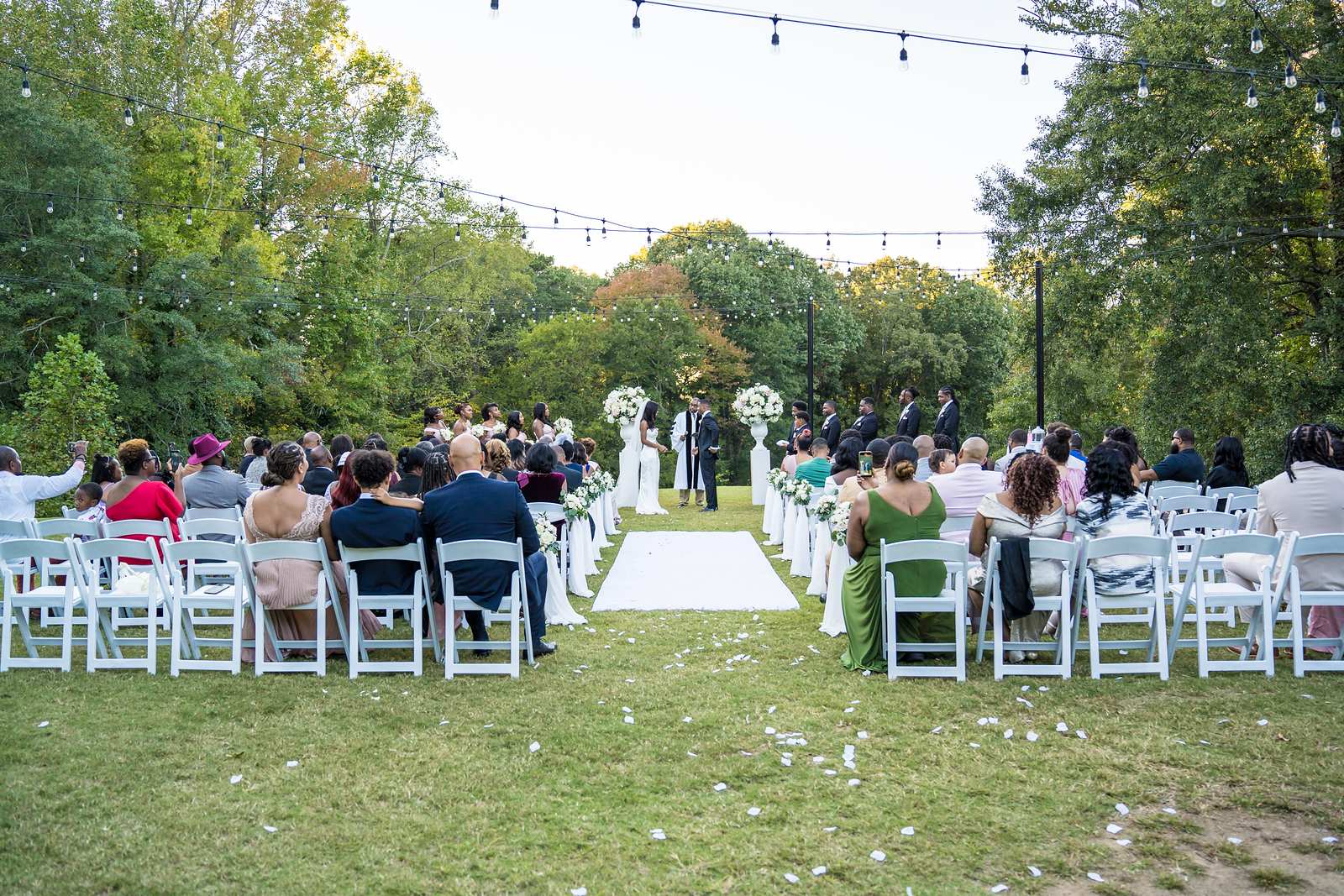 Outdoor ceremony at Chateau Elan seen from the back, with string lights and tall trees overhead