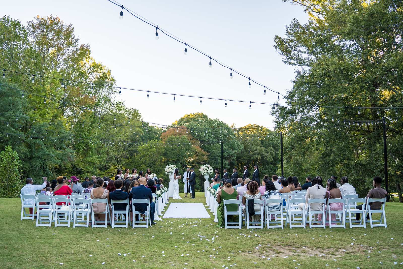 Guests watch the ceremony under string lights on the tree-lined Chateau Elan lawn