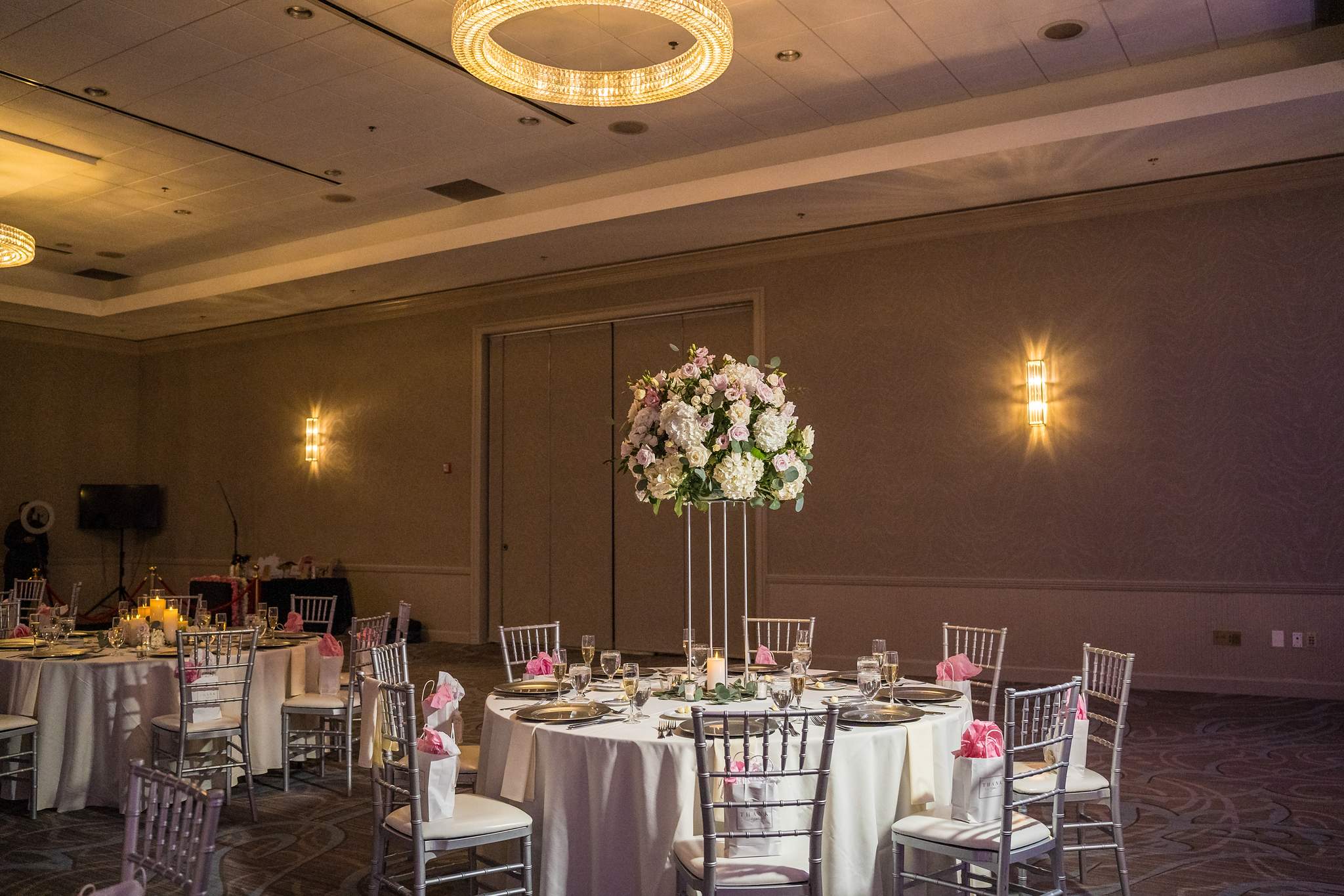 Wide view of the Chateau Elan ballroom with round tables, tall florals and a ring chandelier
