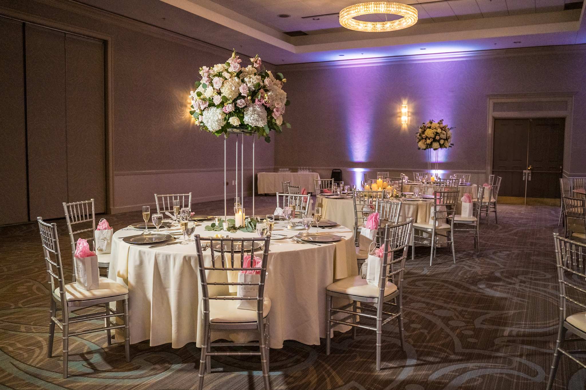 Reception tables with chiavari chairs, pink napkins and a tall floral centerpiece in the ballroom