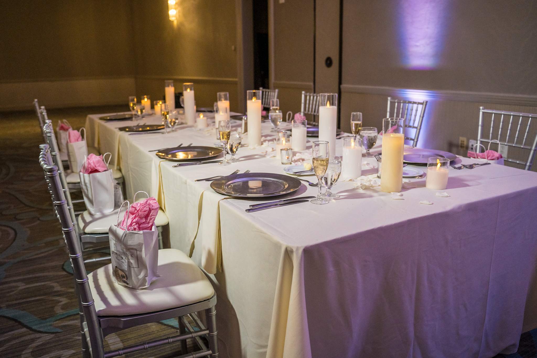 Long reception table set with candles, gold chargers and pink floral accents