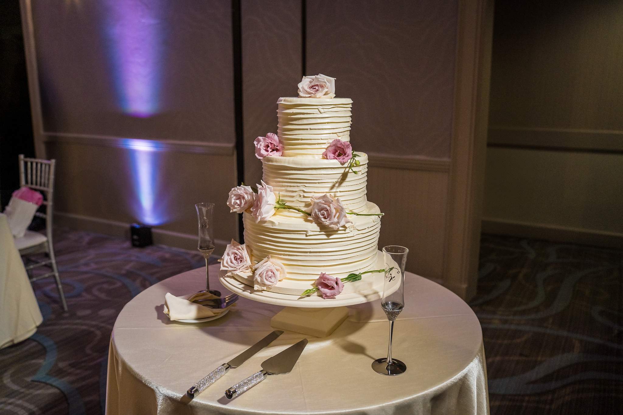 Four-tier white wedding cake decorated with blush roses on a round table