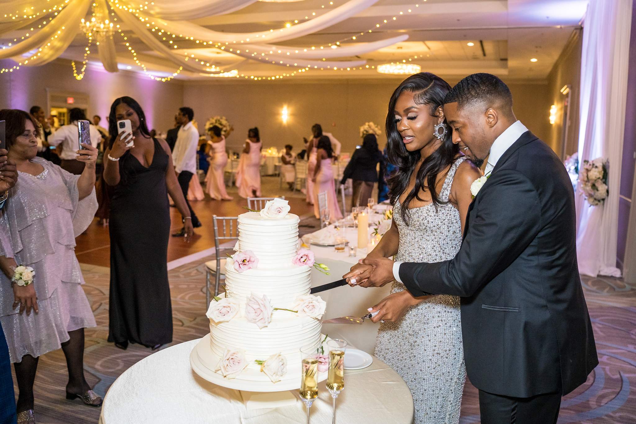 Bride and groom cut their white tiered cake as guests take photos