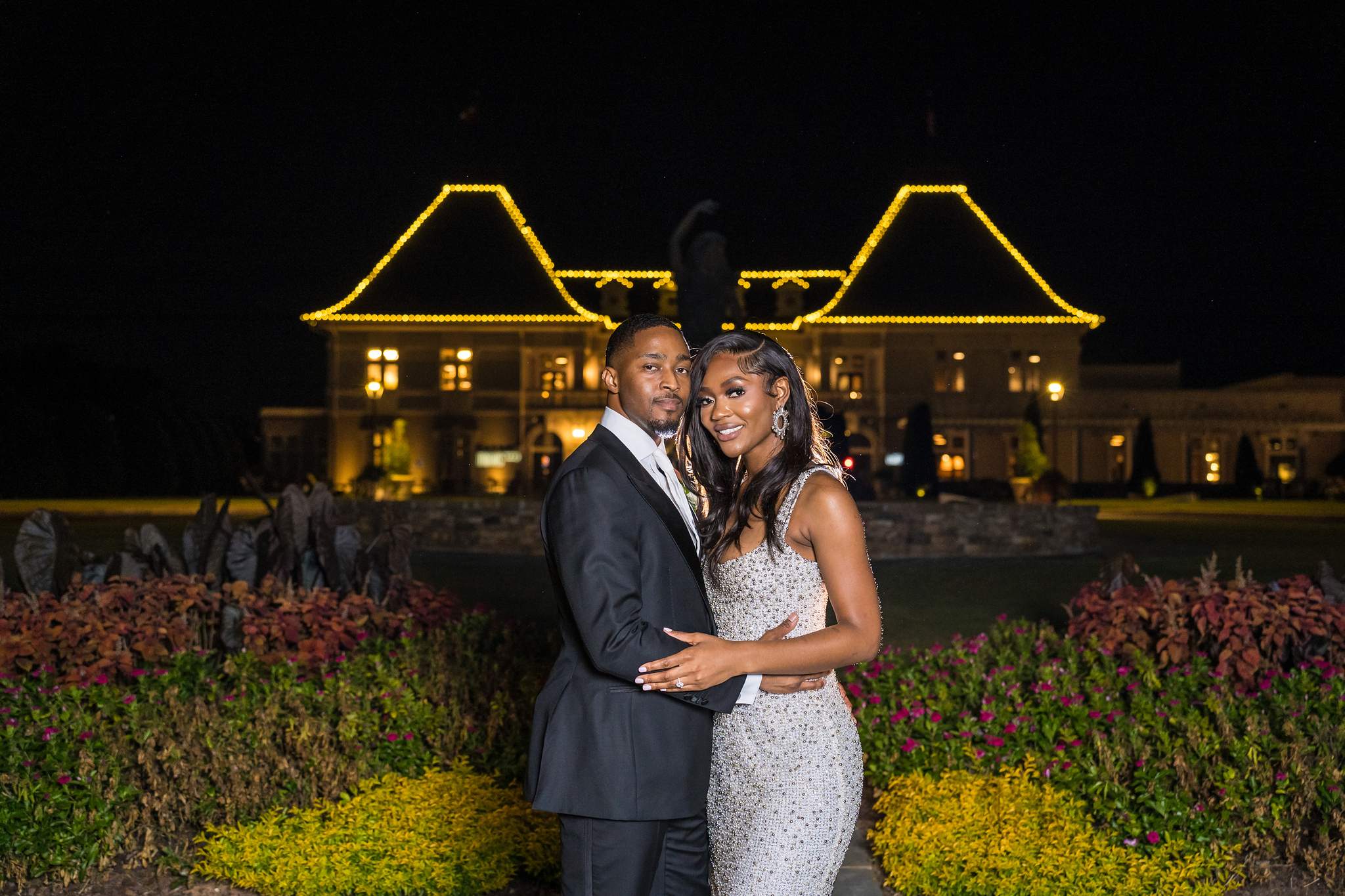 Bride and groom embrace at night in front of the brightly lit Chateau Elan chateau