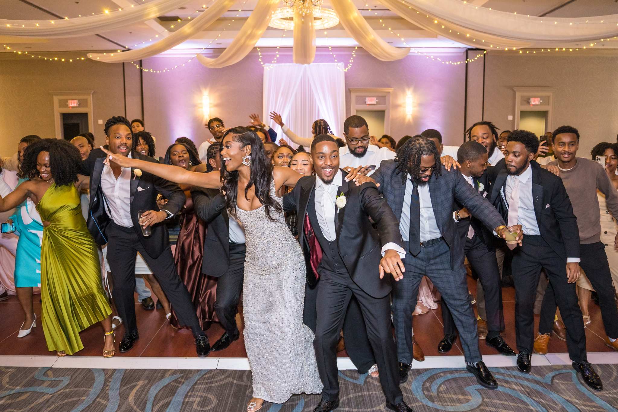 Bride and groom dance in a line with friends during a lively reception dance