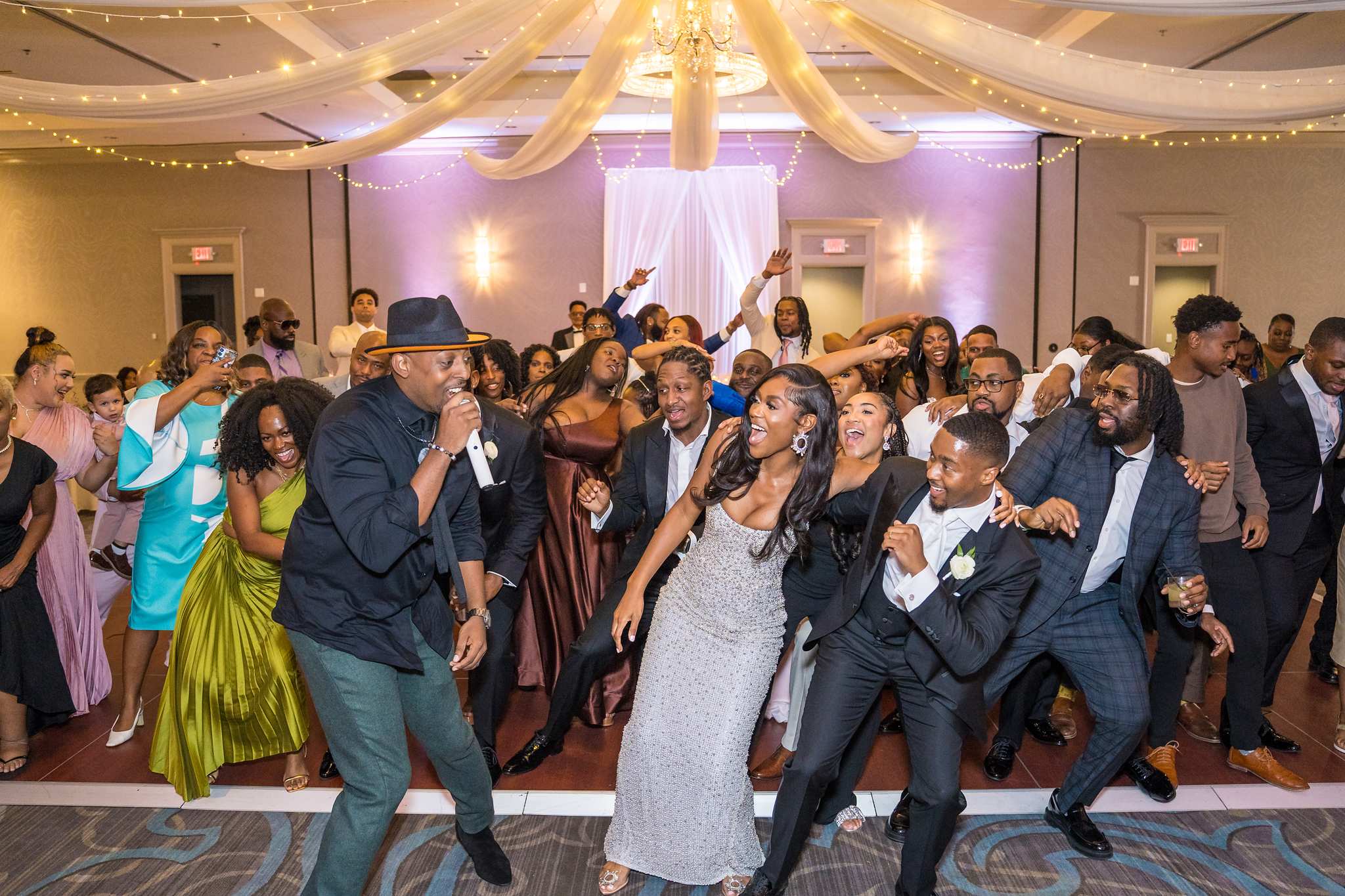 Bride and groom dance shoulder to shoulder with friends on the crowded reception dance floor