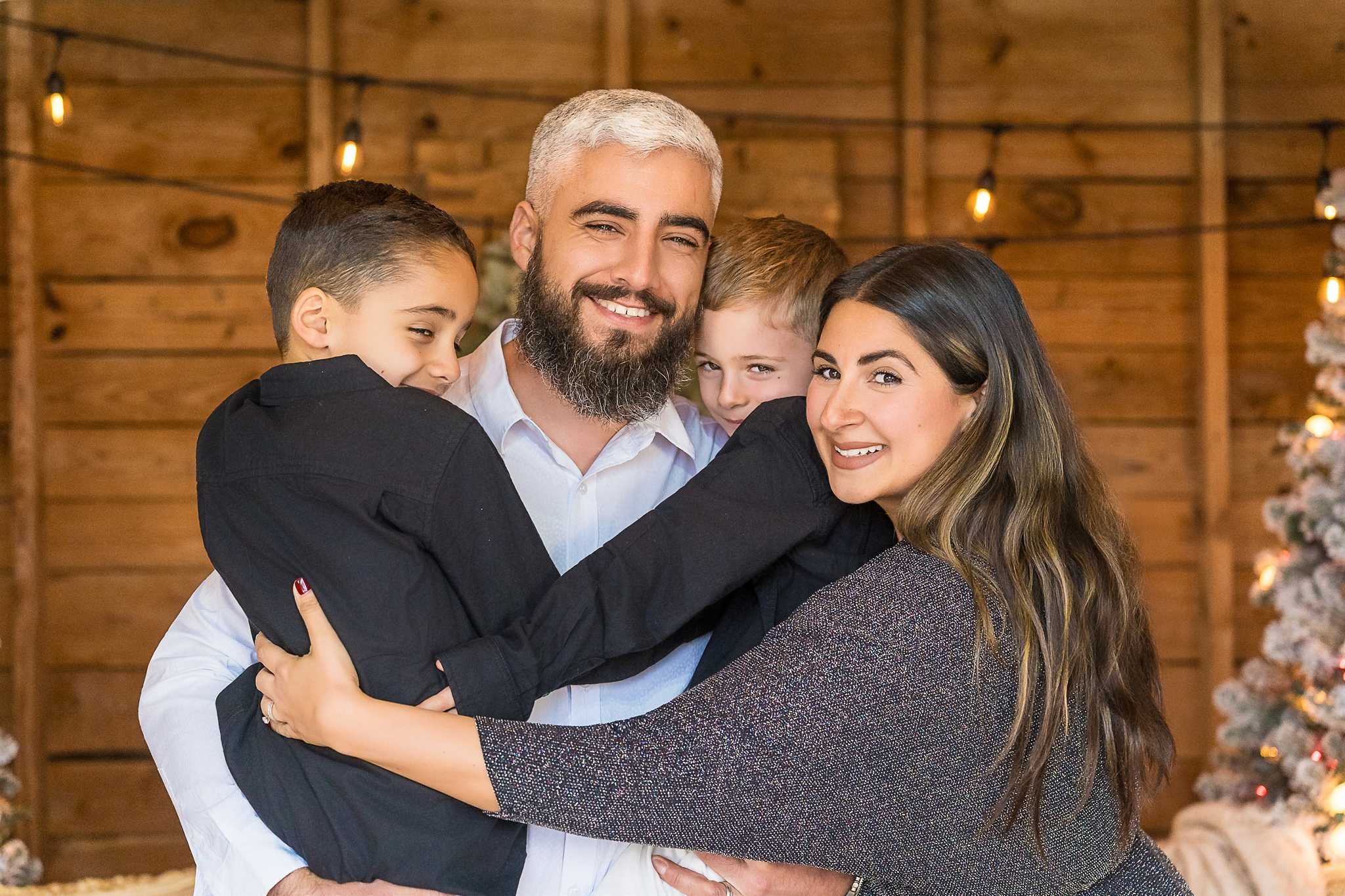 Parents hugging their two sons in black shirts and white pants in the Christmas Barn