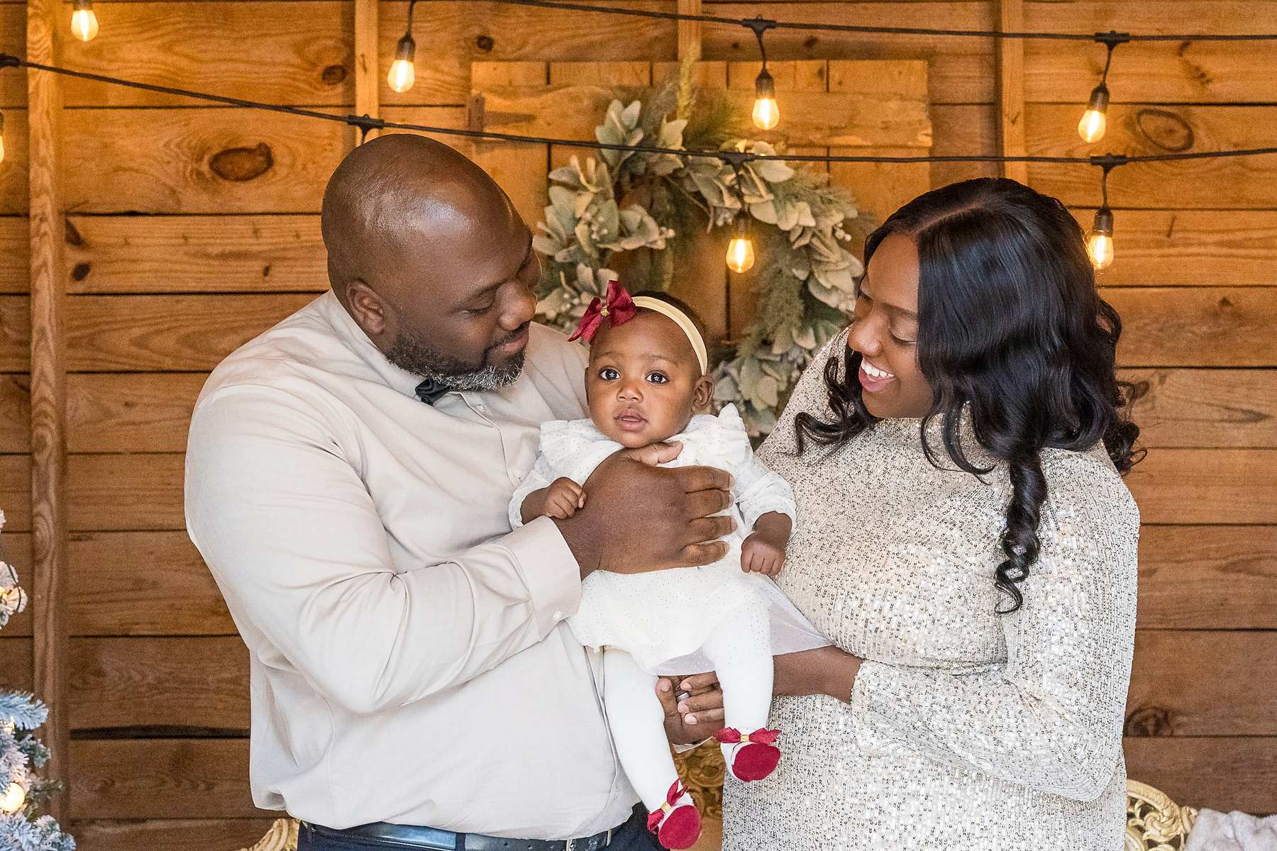 Parents in champagne sequins and ivory holding their baby girl in the Christmas Barn at Prospect Farms