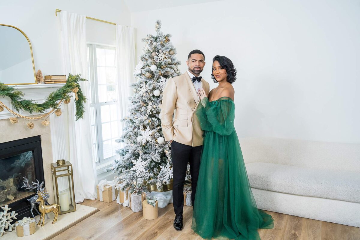 Couple in formal holiday wear beside a white flocked Christmas tree