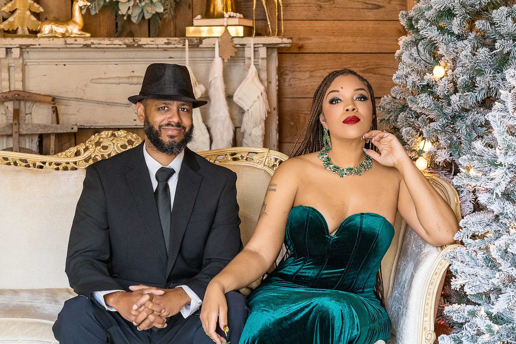 Couple in an emerald velvet gown and navy suit on the white settee in the Christmas Barn