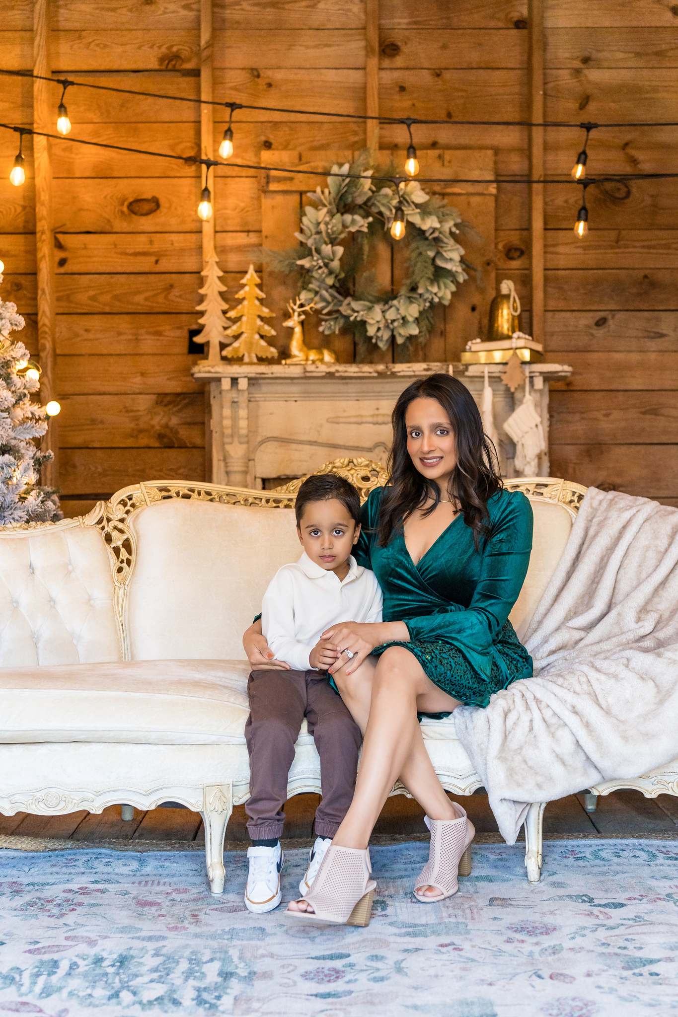 Mother in an emerald velvet dress with her son on the white settee in the Christmas Barn