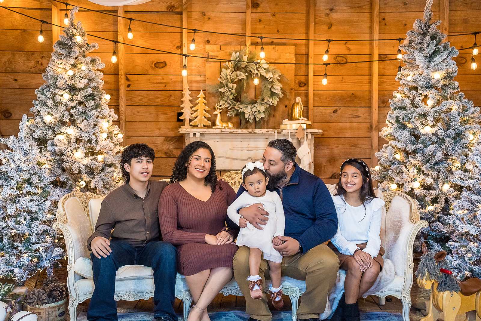 Family in mauve, navy, brown and white on the white settee in the Christmas Barn at Prospect Farms