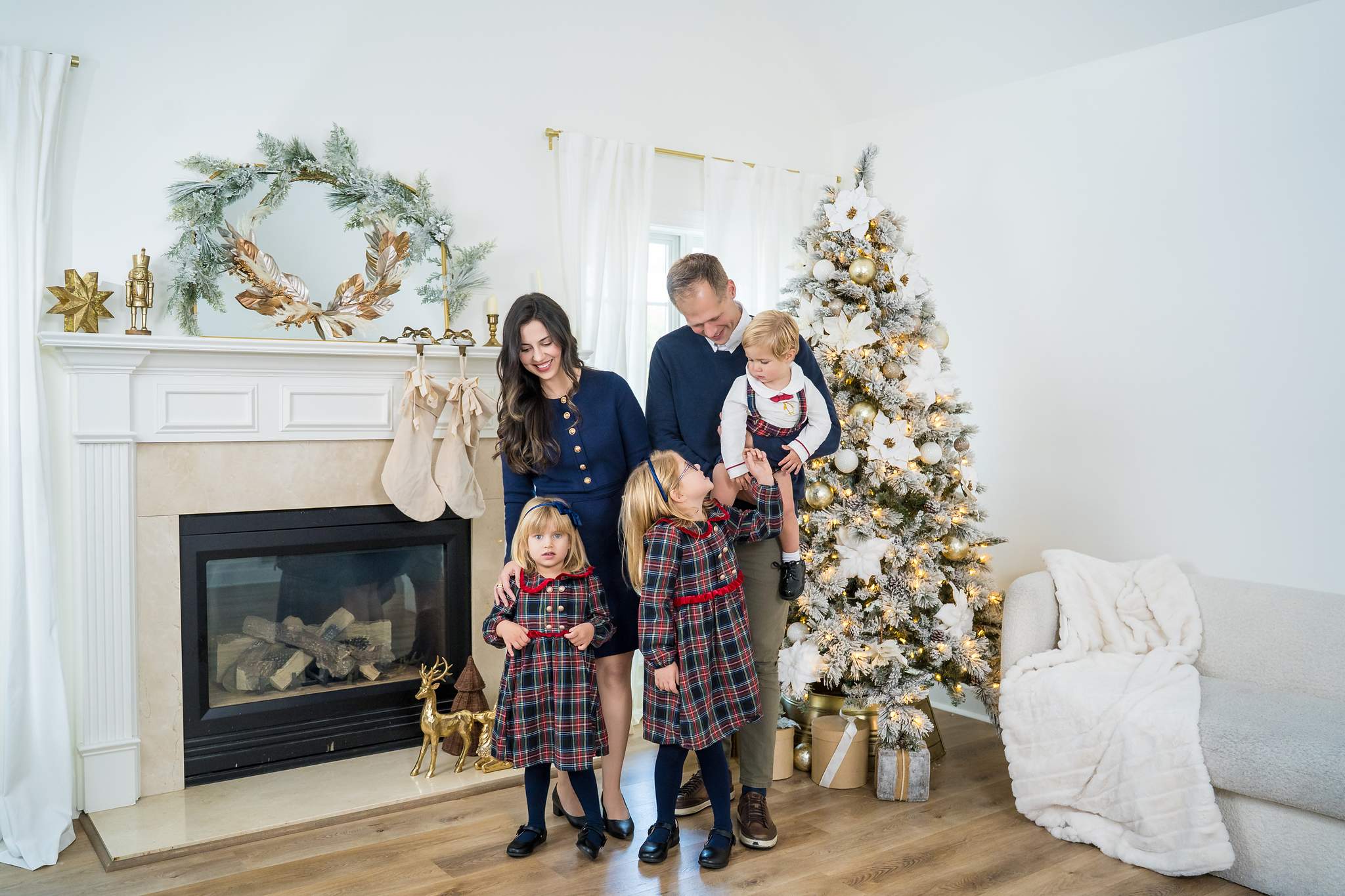 Family in navy and red tartan standing by the fireplace and Christmas tree