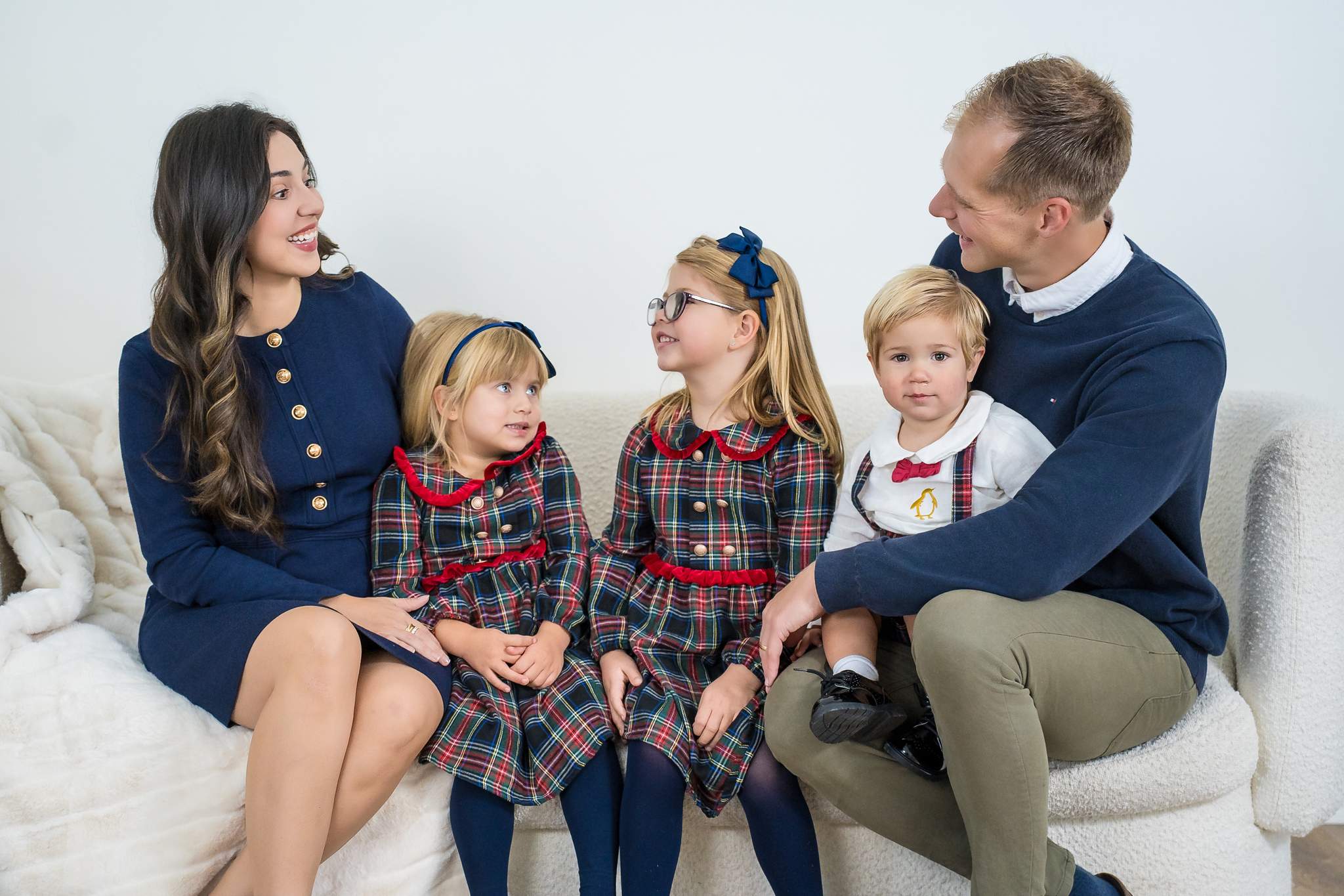 Parents in navy with their children in matching red and navy tartan on a white sofa