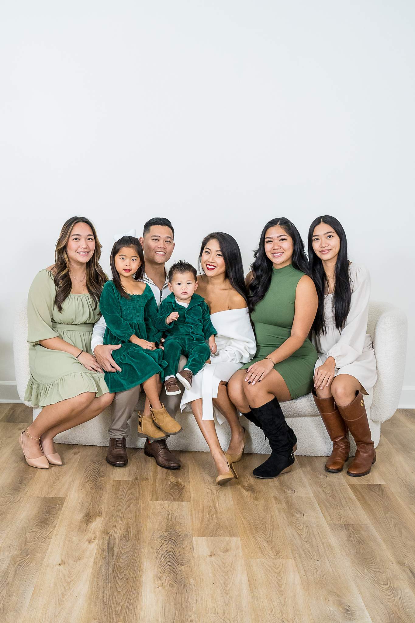 Extended family in sage, emerald and cream sitting together beside a Christmas tree