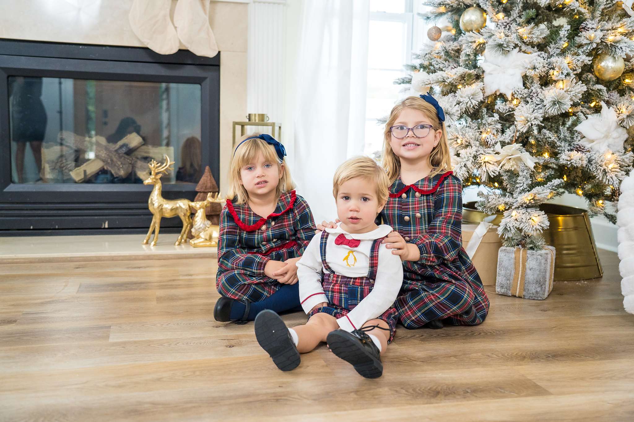 Three siblings in matching navy and red tartan sitting by the fireplace