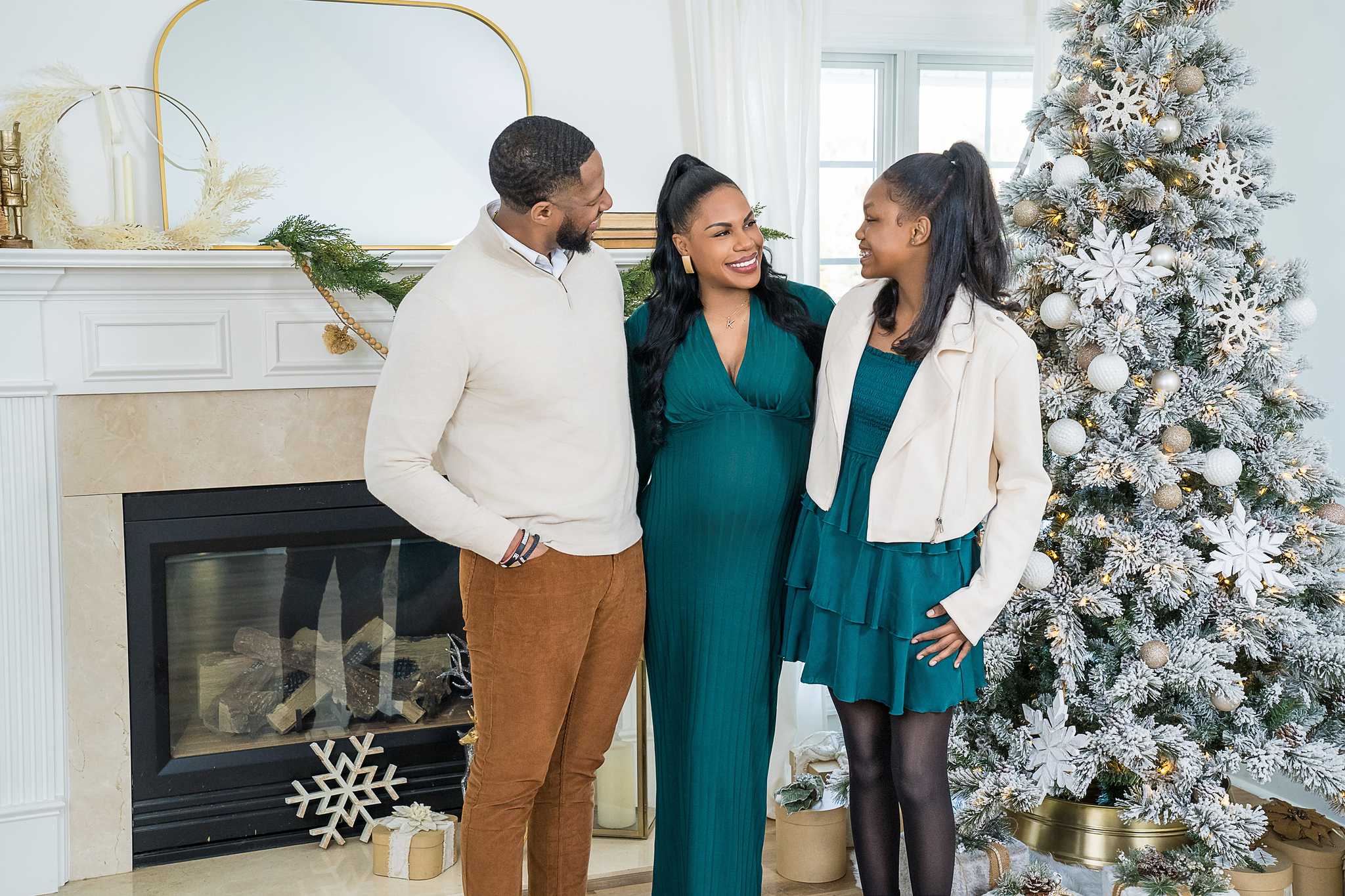 Family in teal, cream and camel by the fireplace and Christmas tree