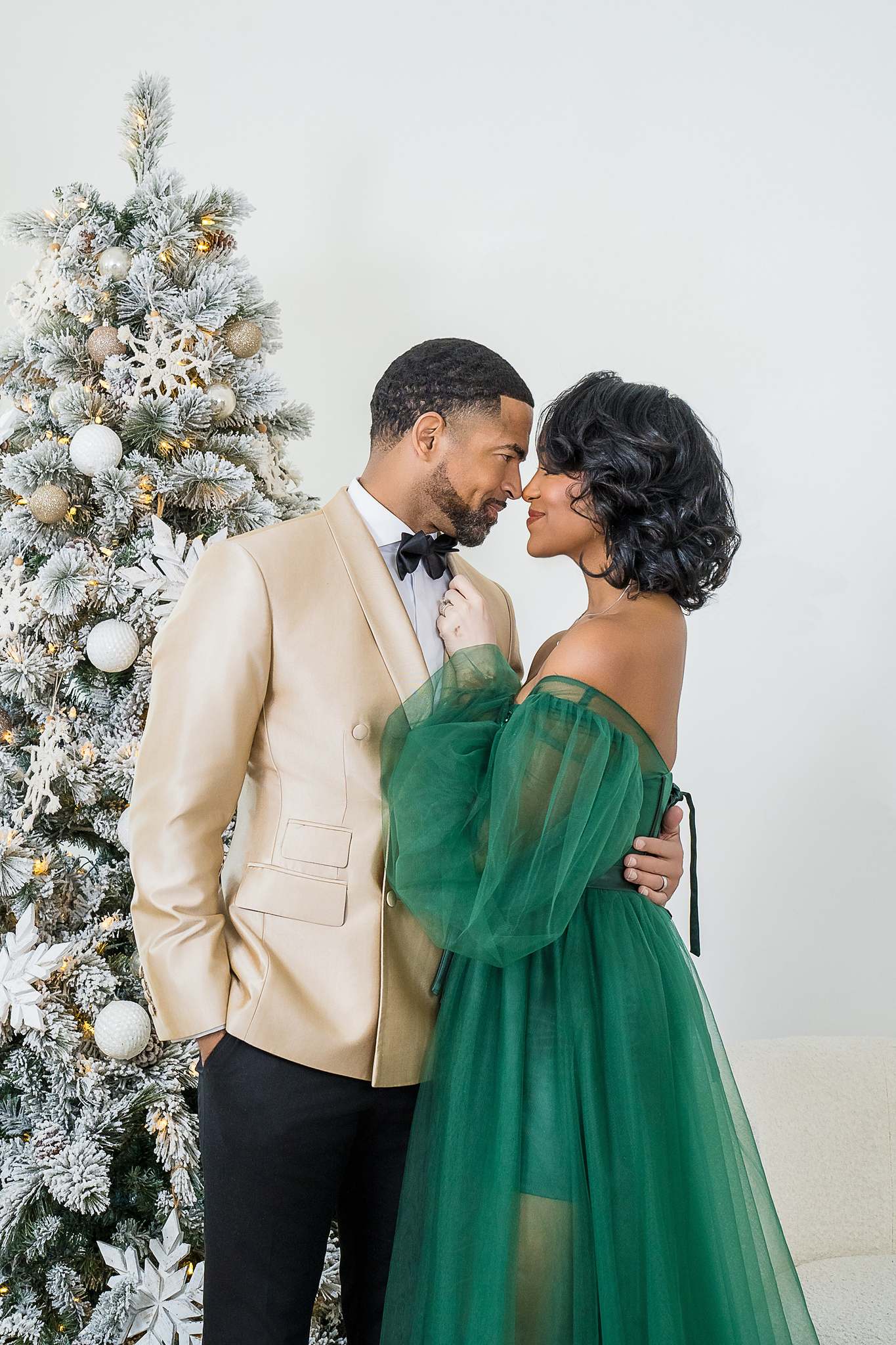 Couple in an emerald green gown and cream jacket by a flocked Christmas tree