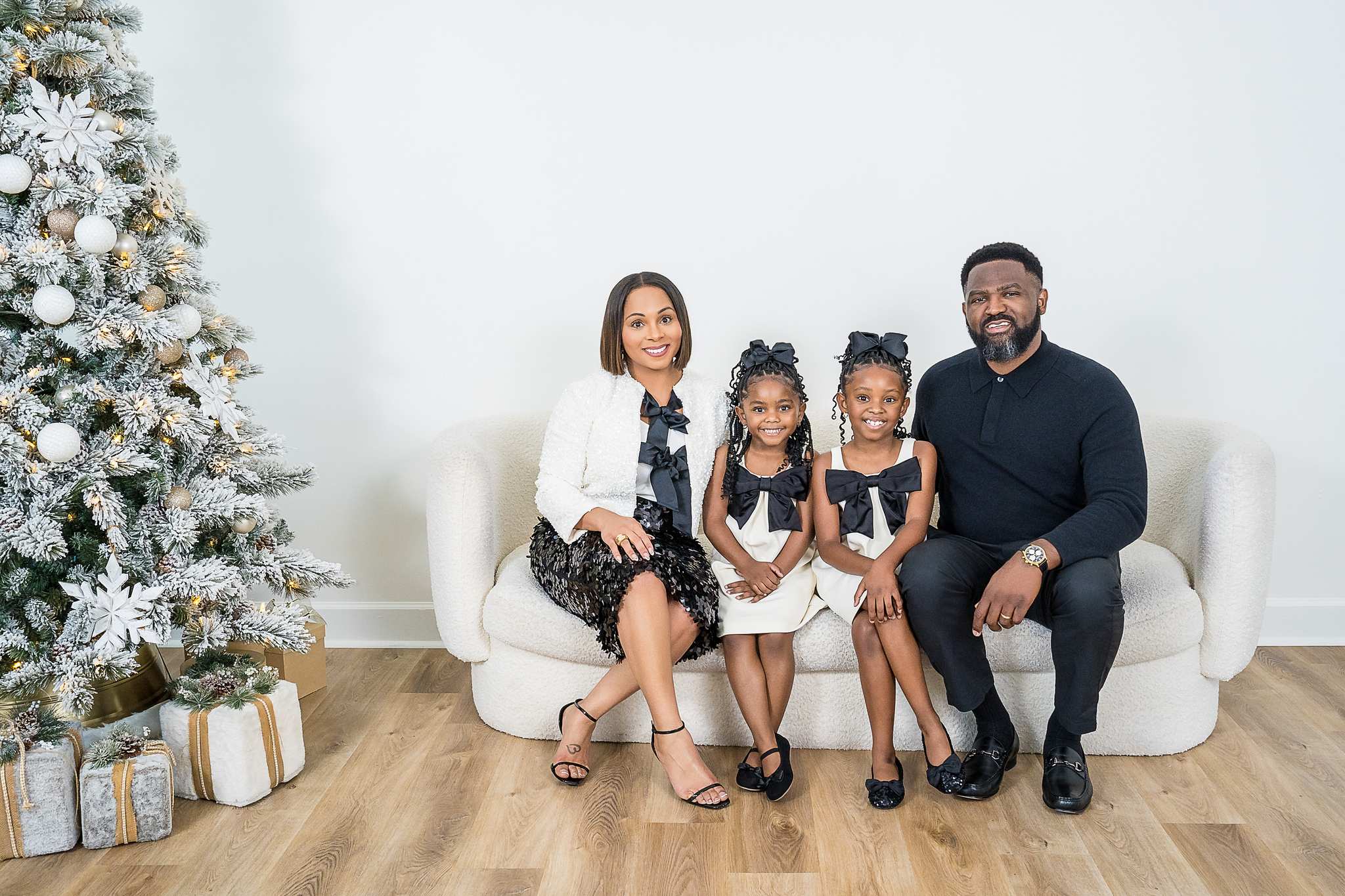 Family in green and cream outfits on a white couch beside a Christmas tree