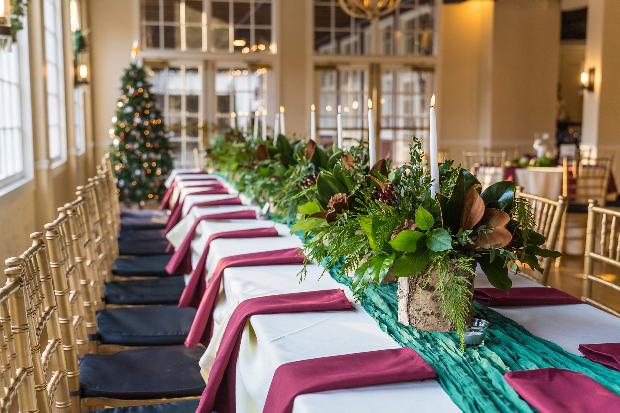 Long head table with greenery garland, burgundy napkins and a Christmas tree