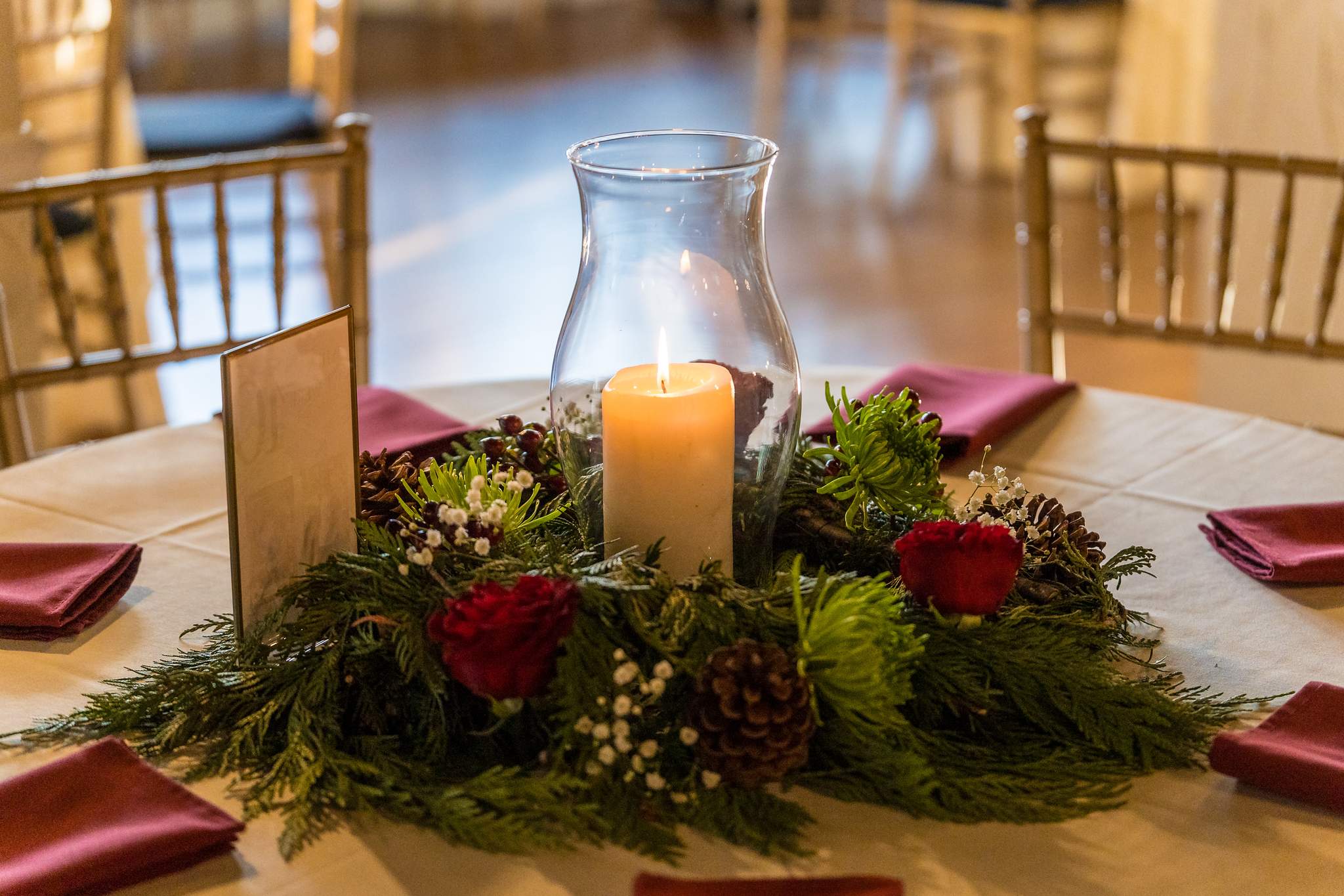Candle centerpiece with evergreen and red berries on a Christmas wedding reception table