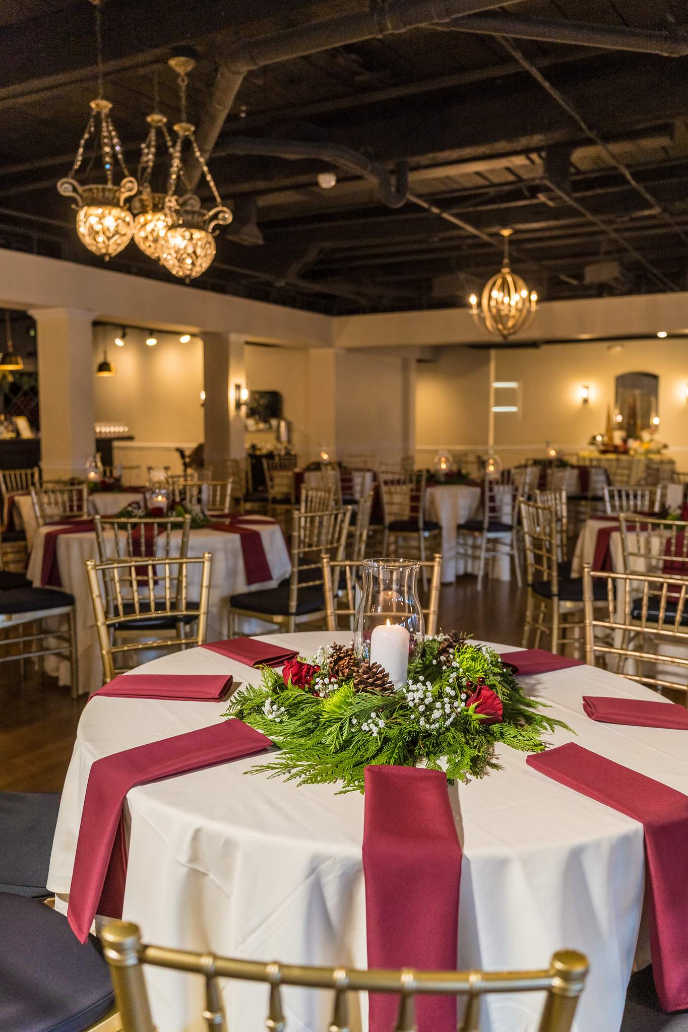 Round reception table with a burgundy runner and holiday greenery
