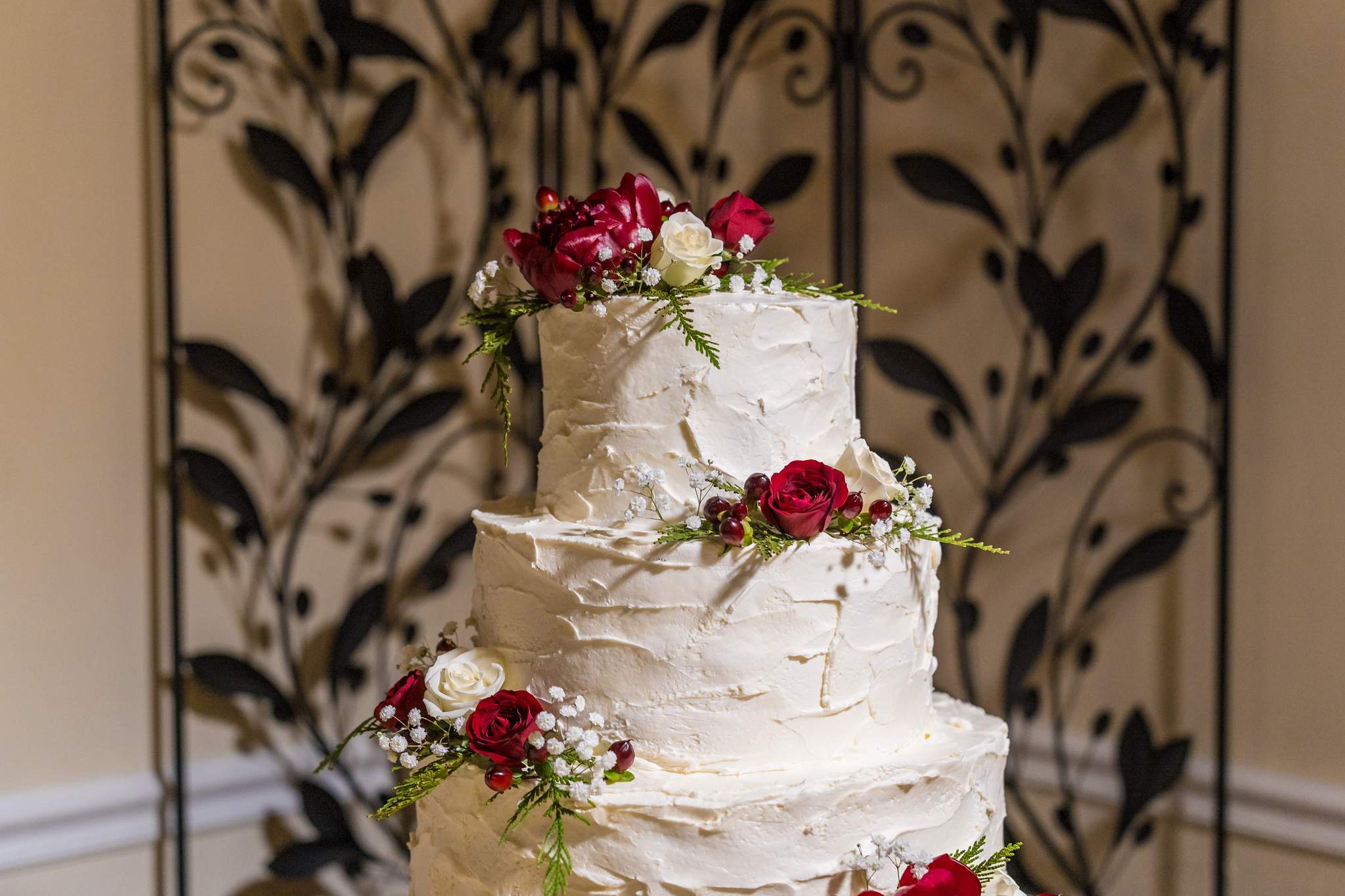 White buttercream wedding cake with red roses and greenery