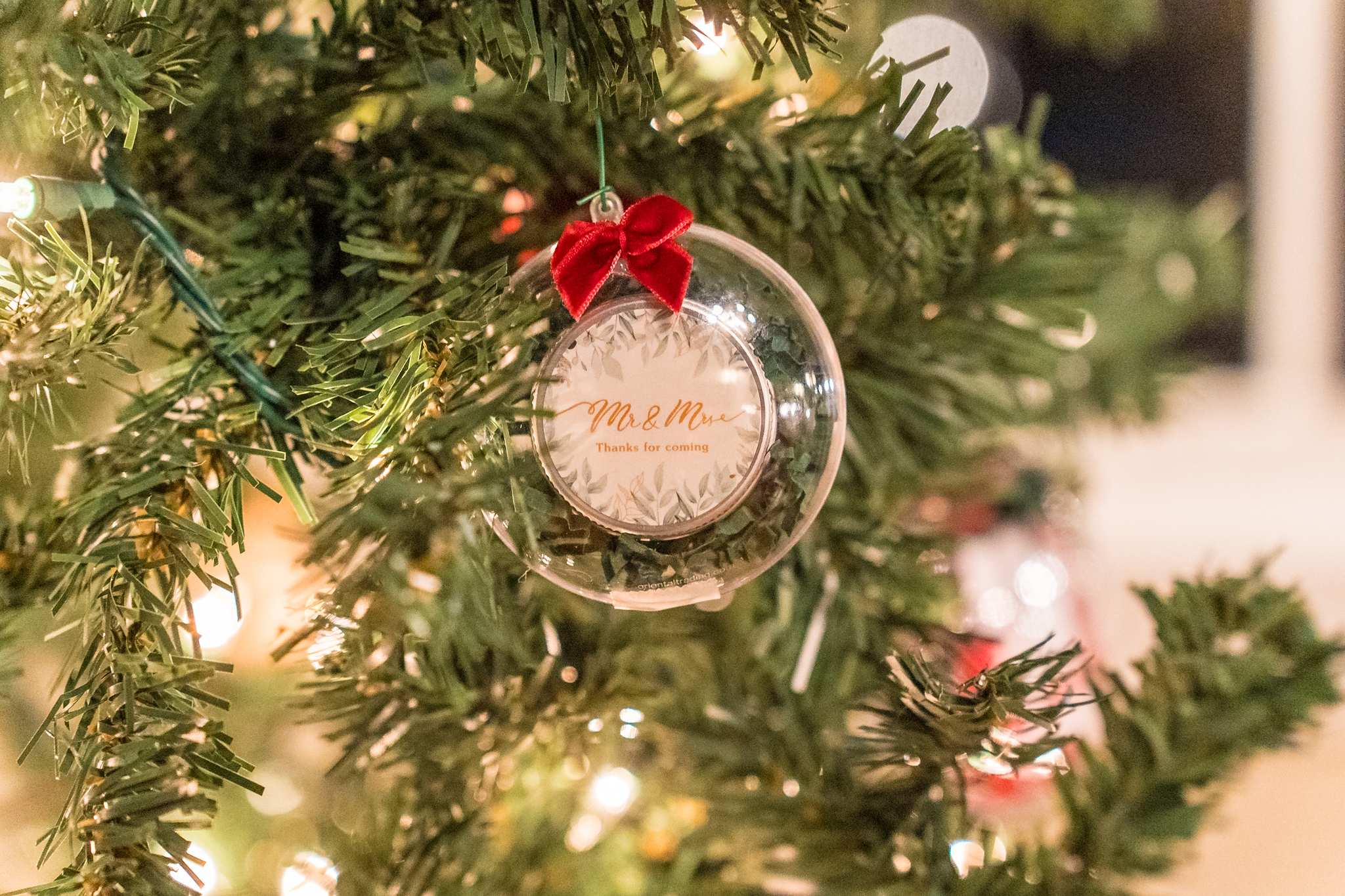 Custom wedding ornament with red bow on a lit Christmas tree