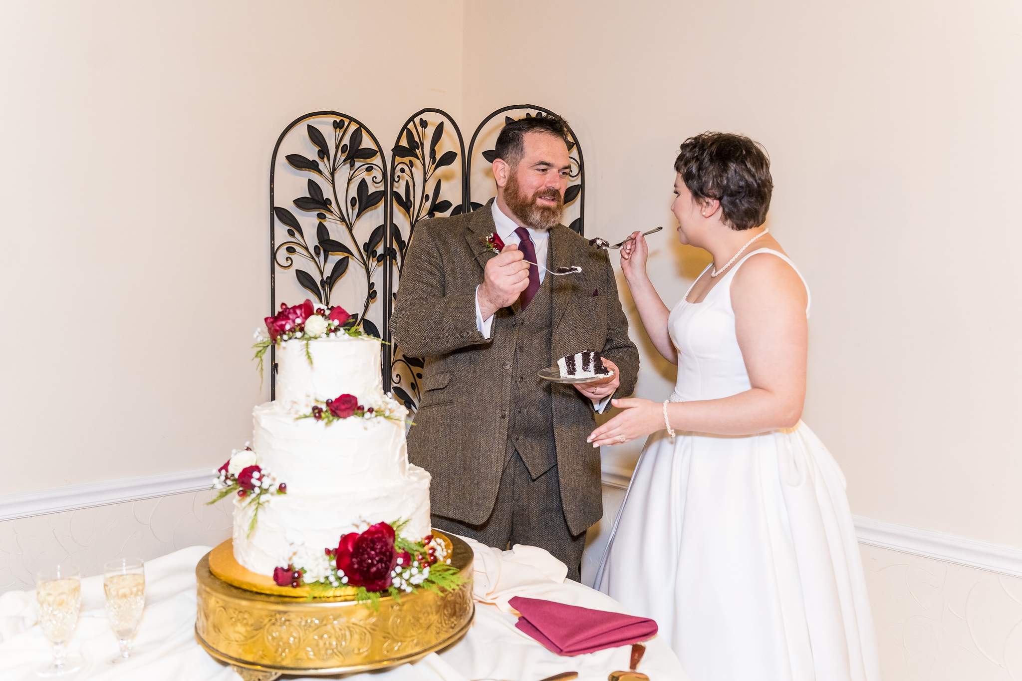 Couple cutting a white wedding cake with red flowers