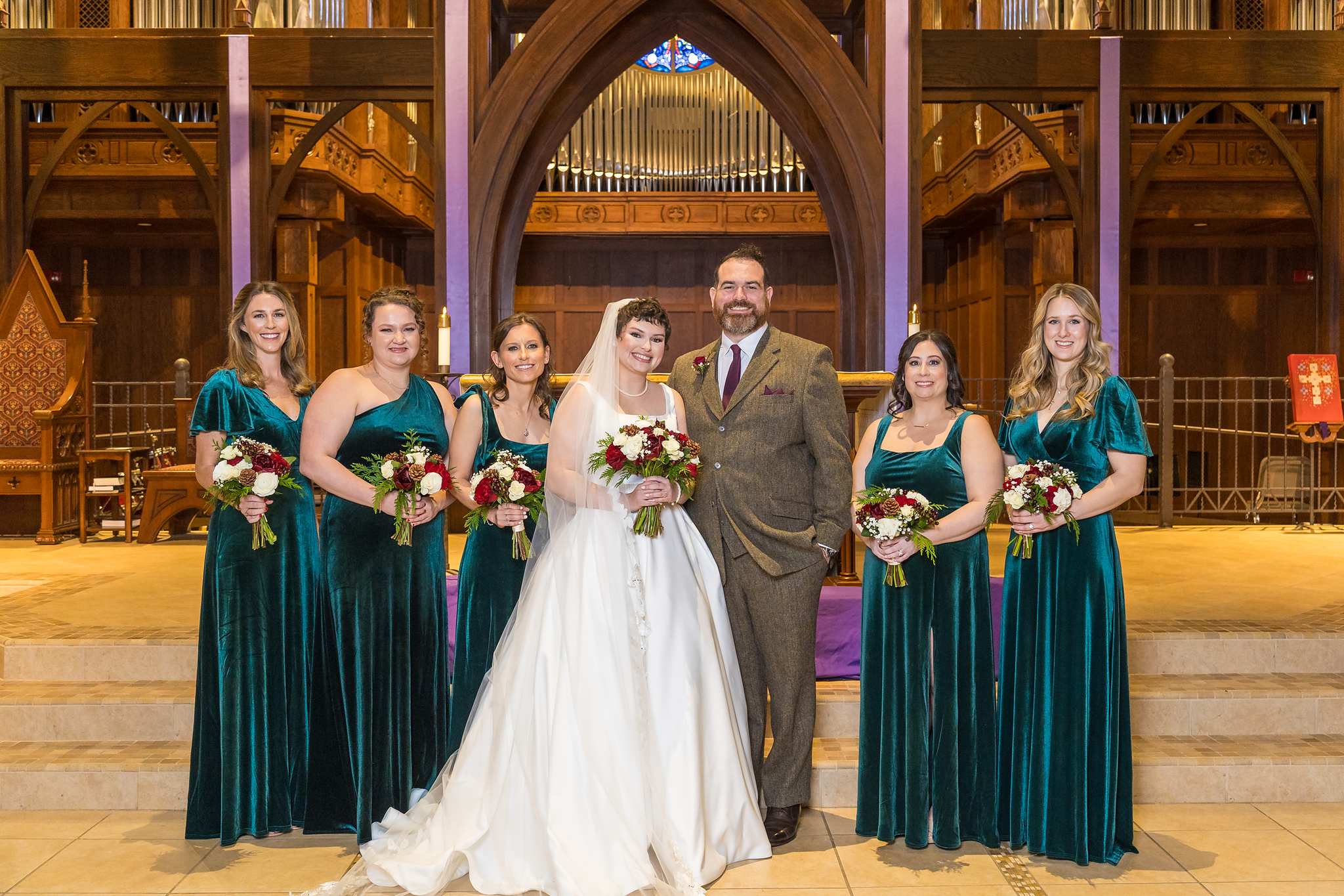 Bride and groom with bridesmaids in emerald velvet dresses at a church altar