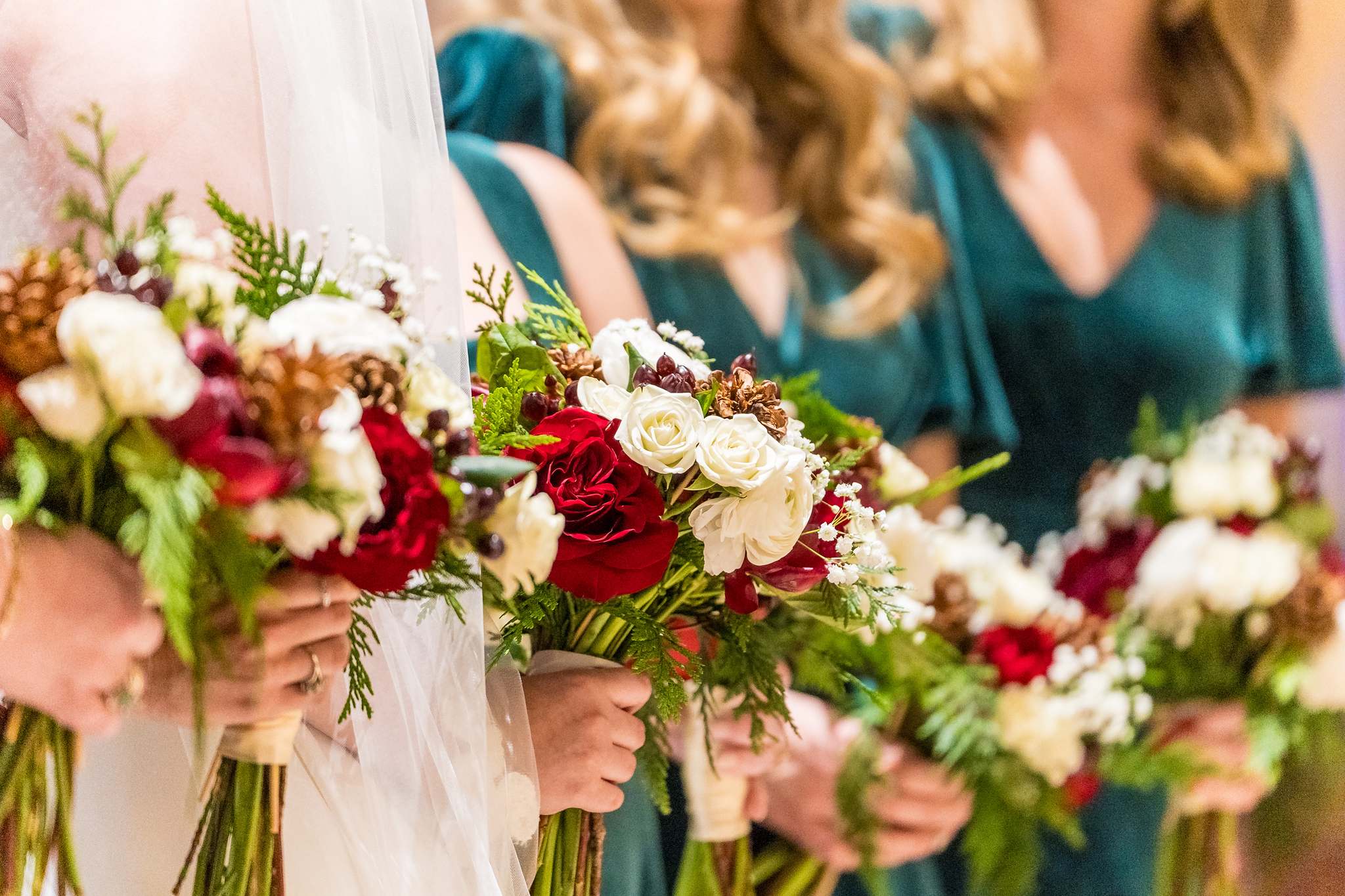 Bridesmaids holding red and white bouquets with greenery