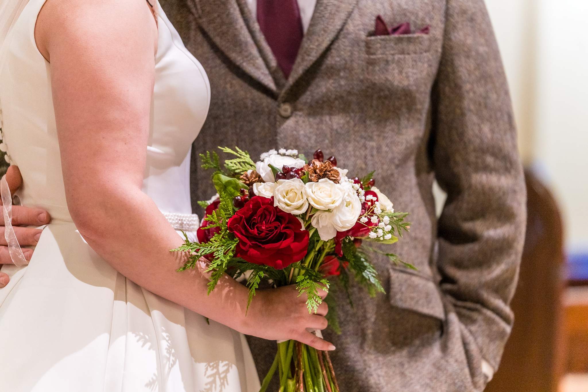 Bride holding a red and ivory bouquet next to the groom in a tweed suit