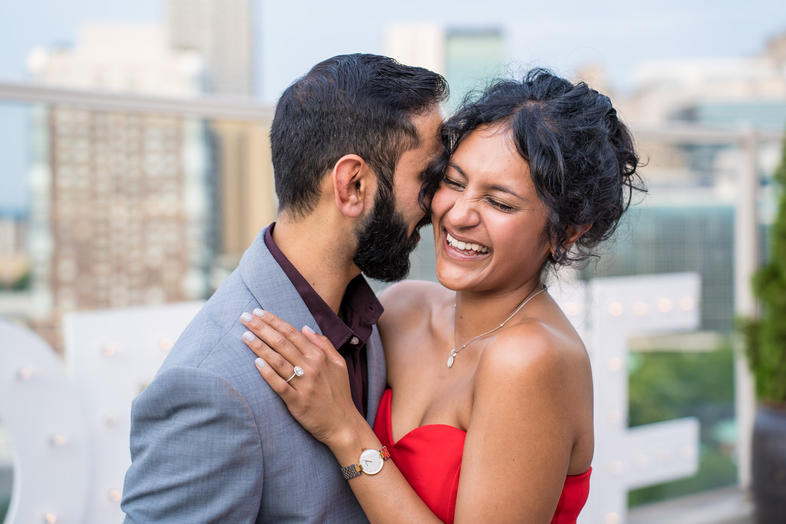 Newly engaged woman laughing as her fiancé leans in close, her engagement ring visible