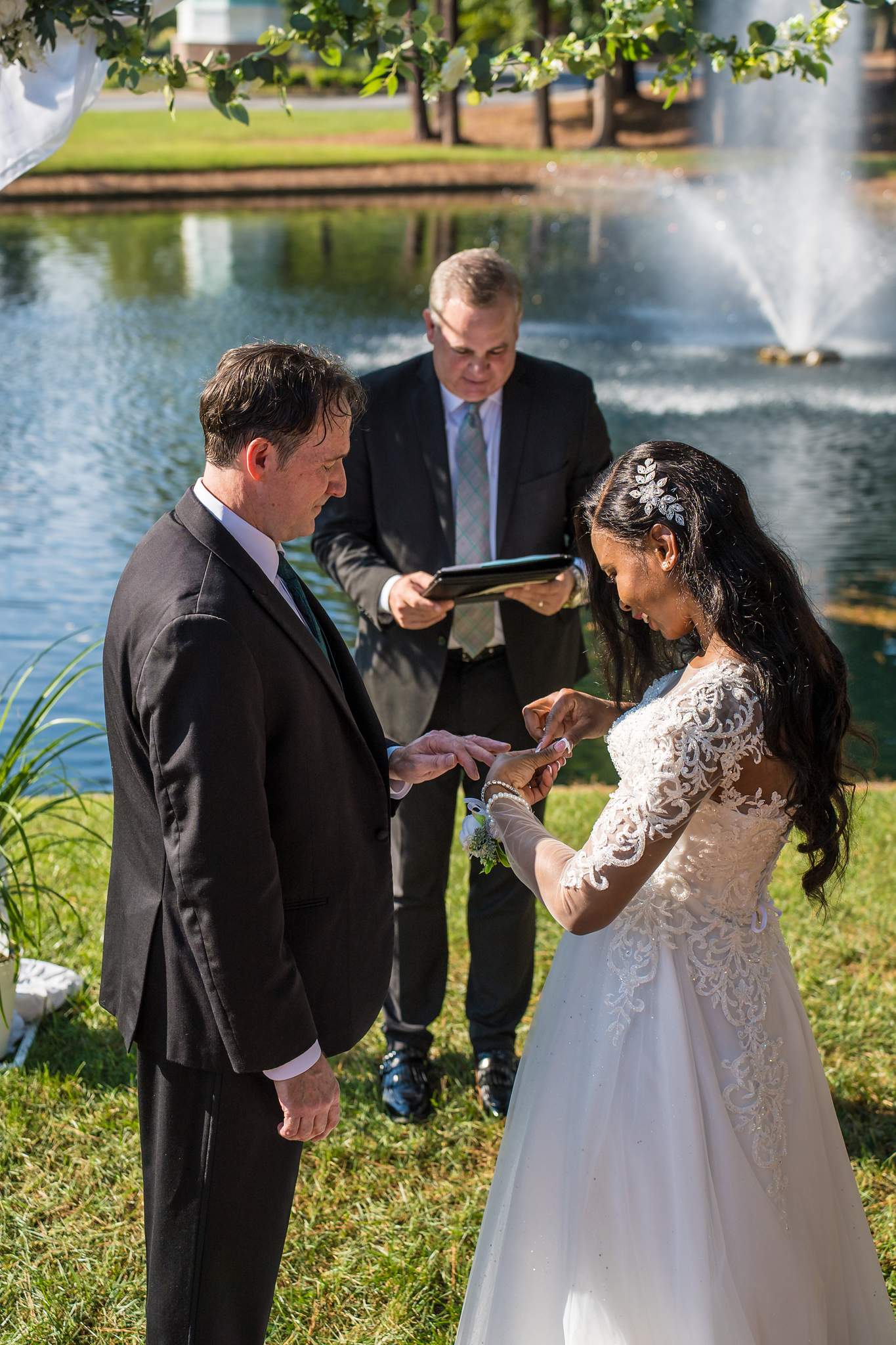 Couple exchanging rings with the officiant by the fountain