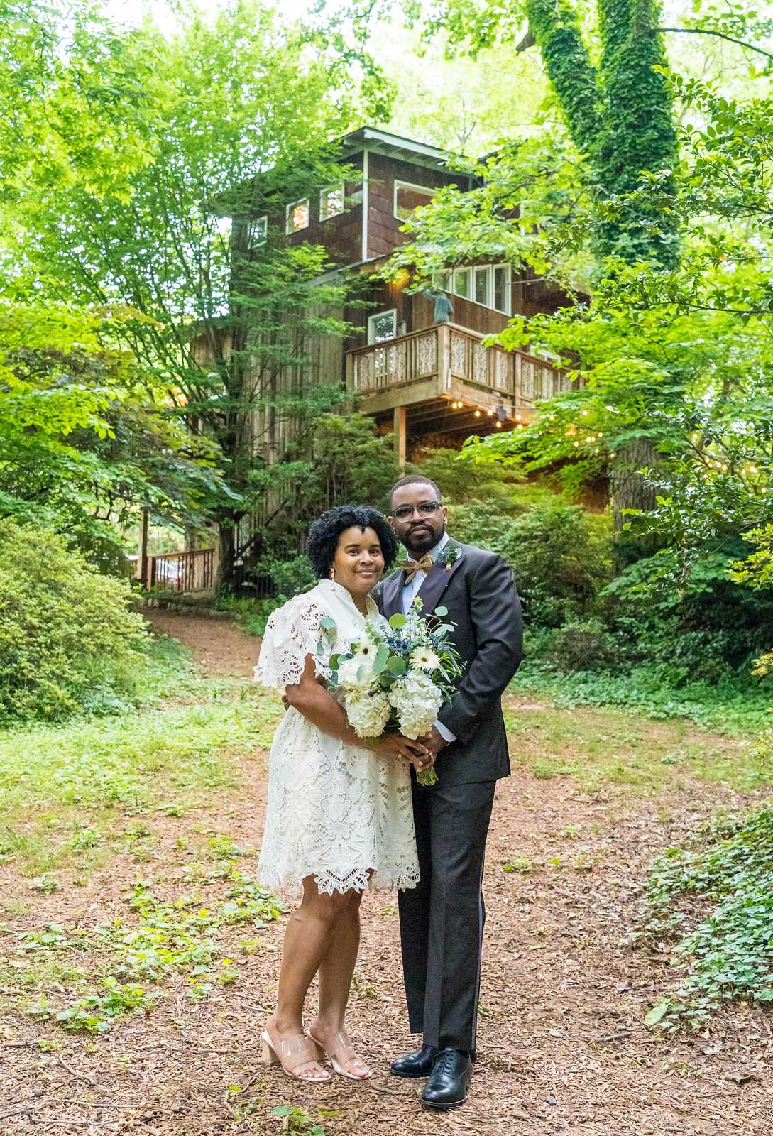 Couple portrait on a wooded path with a treehouse behind them