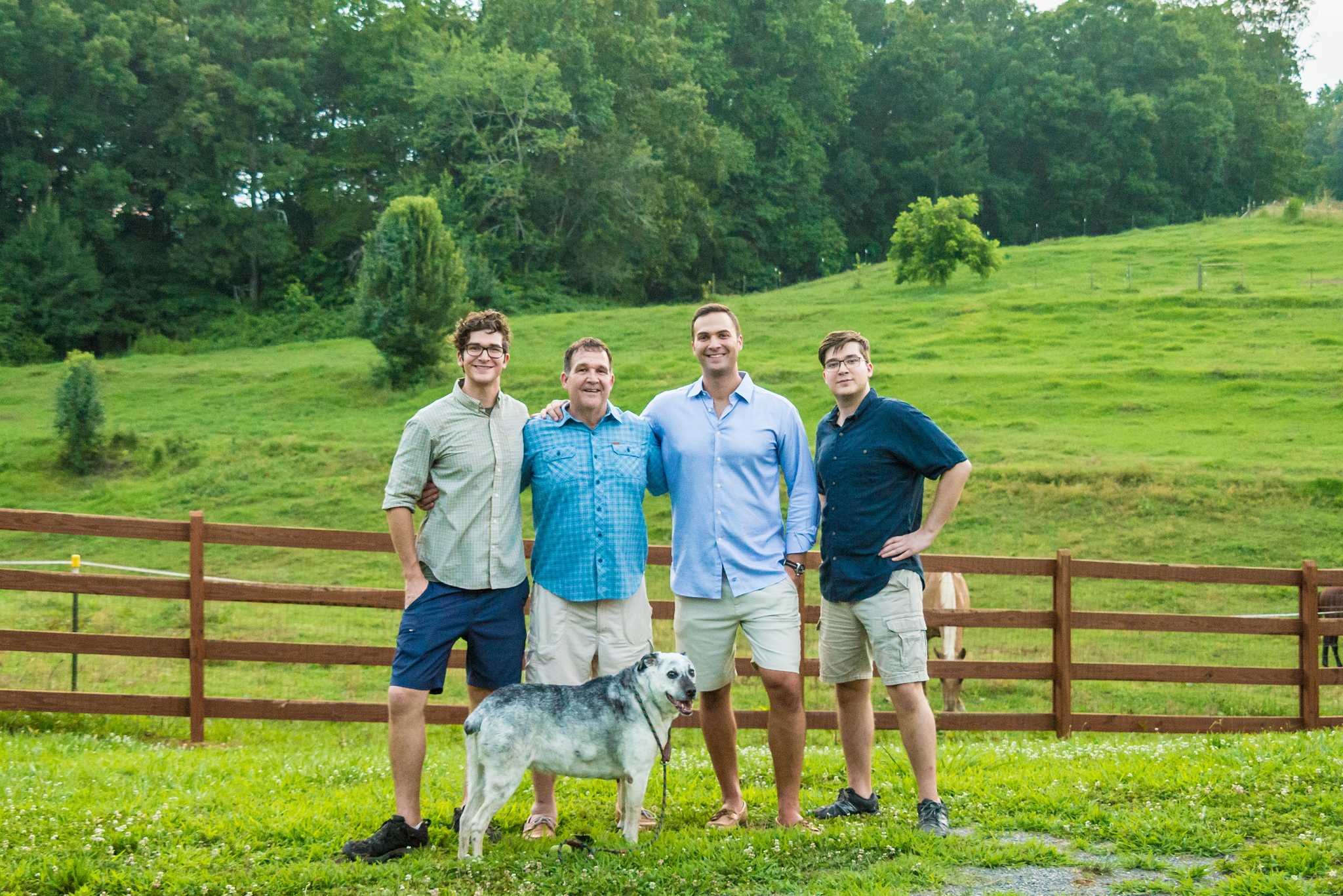 Four young men posing with a white dog in front of a wooden fence and rolling pasture at a park near Marietta