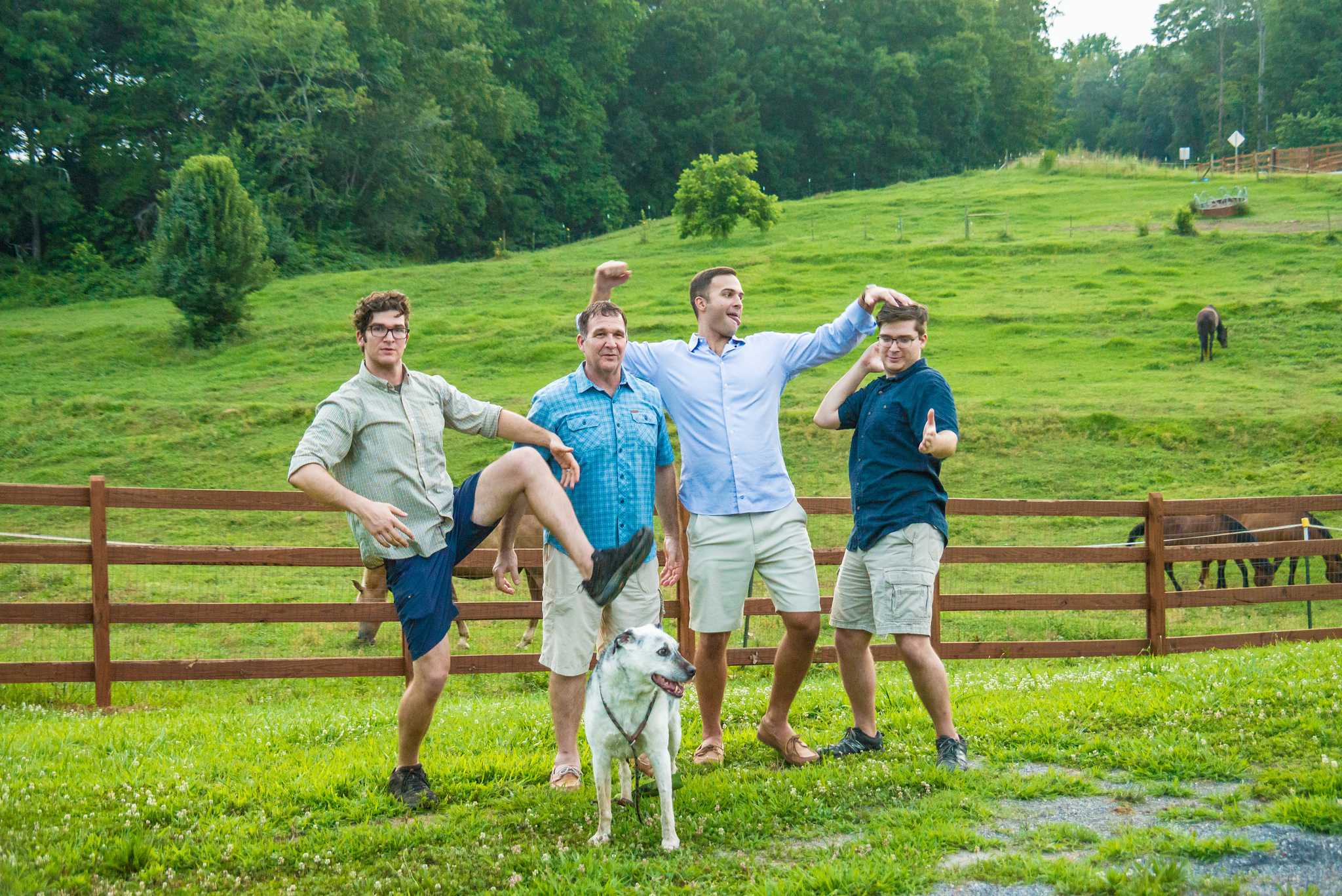Four friends striking playful poses with their white dog in front of a pasture fence near Marietta