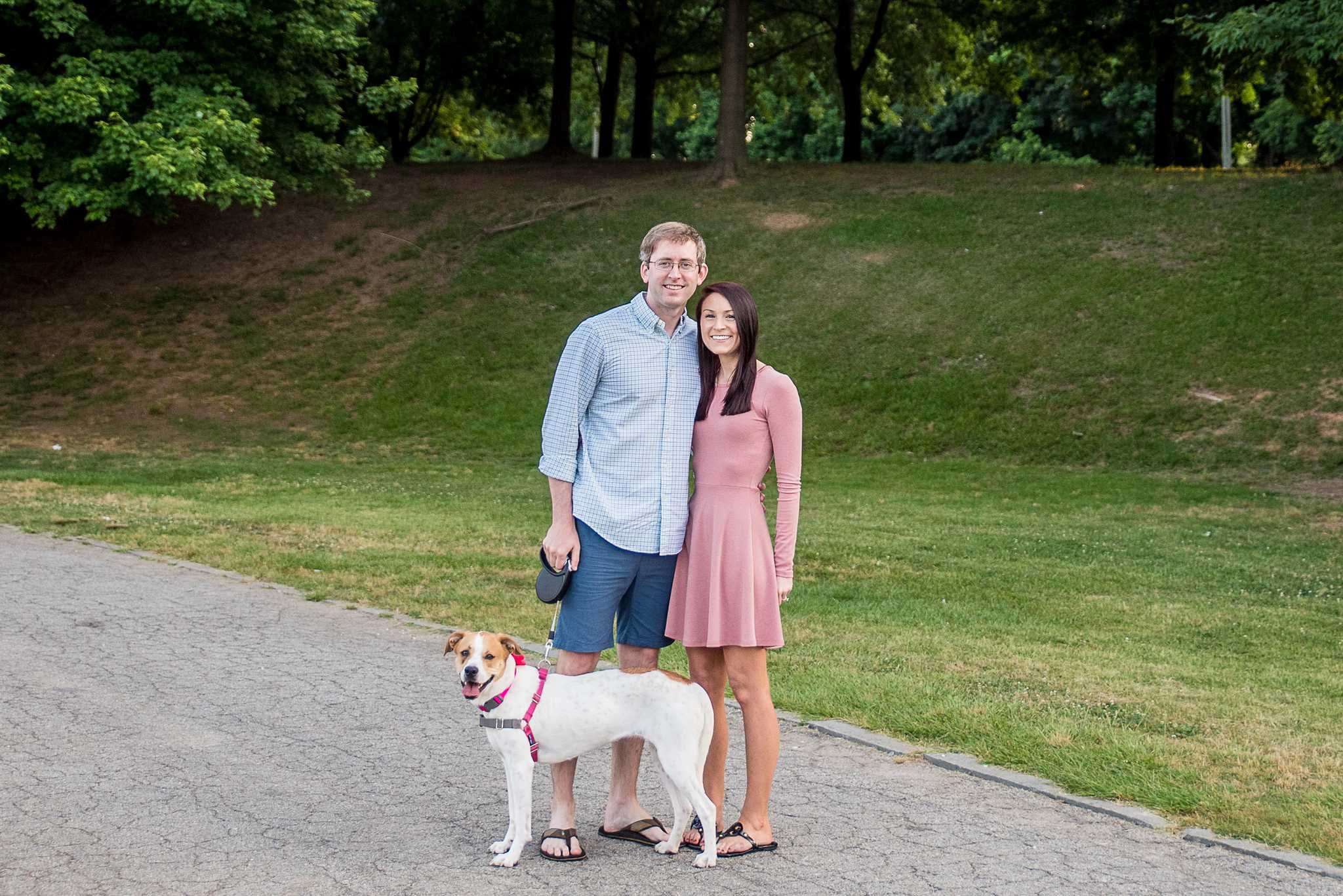 Couple standing on a paved path with their dog sitting beside them at Piedmont Park
