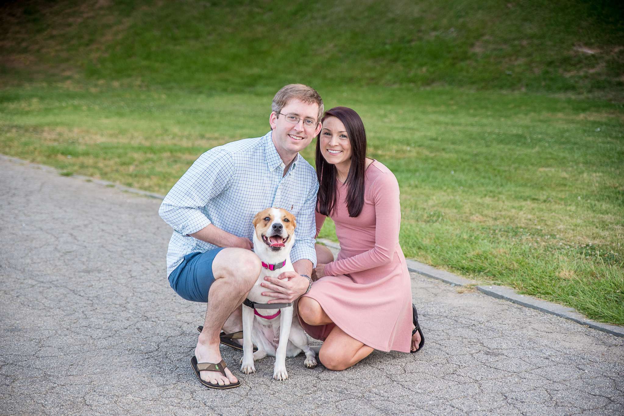 Couple kneeling with their dog on a park path in front of a grassy hill at Piedmont Park
