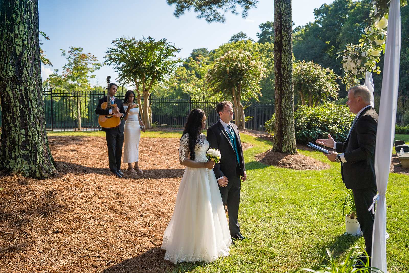 Wide view of a small outdoor ceremony with guests and a guitarist