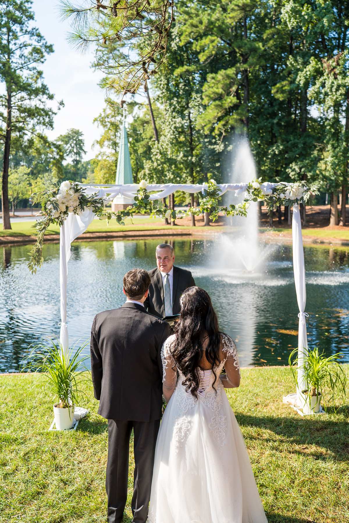 Couple with the officiant under the arch with the fountain behind them