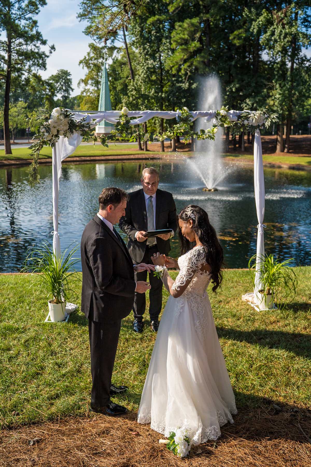 Couple and officiant under the floral arch by the pond