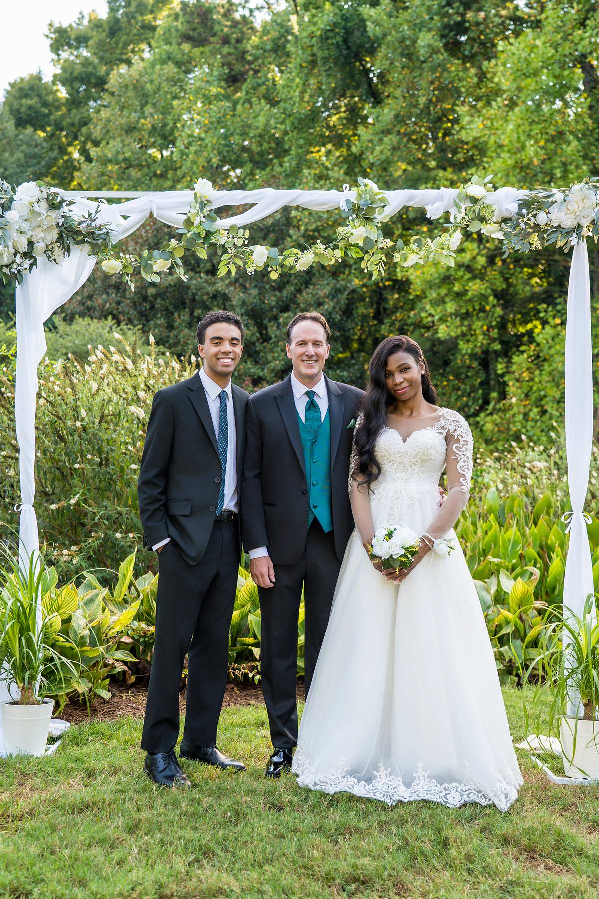Couple and officiant smiling under the floral arch