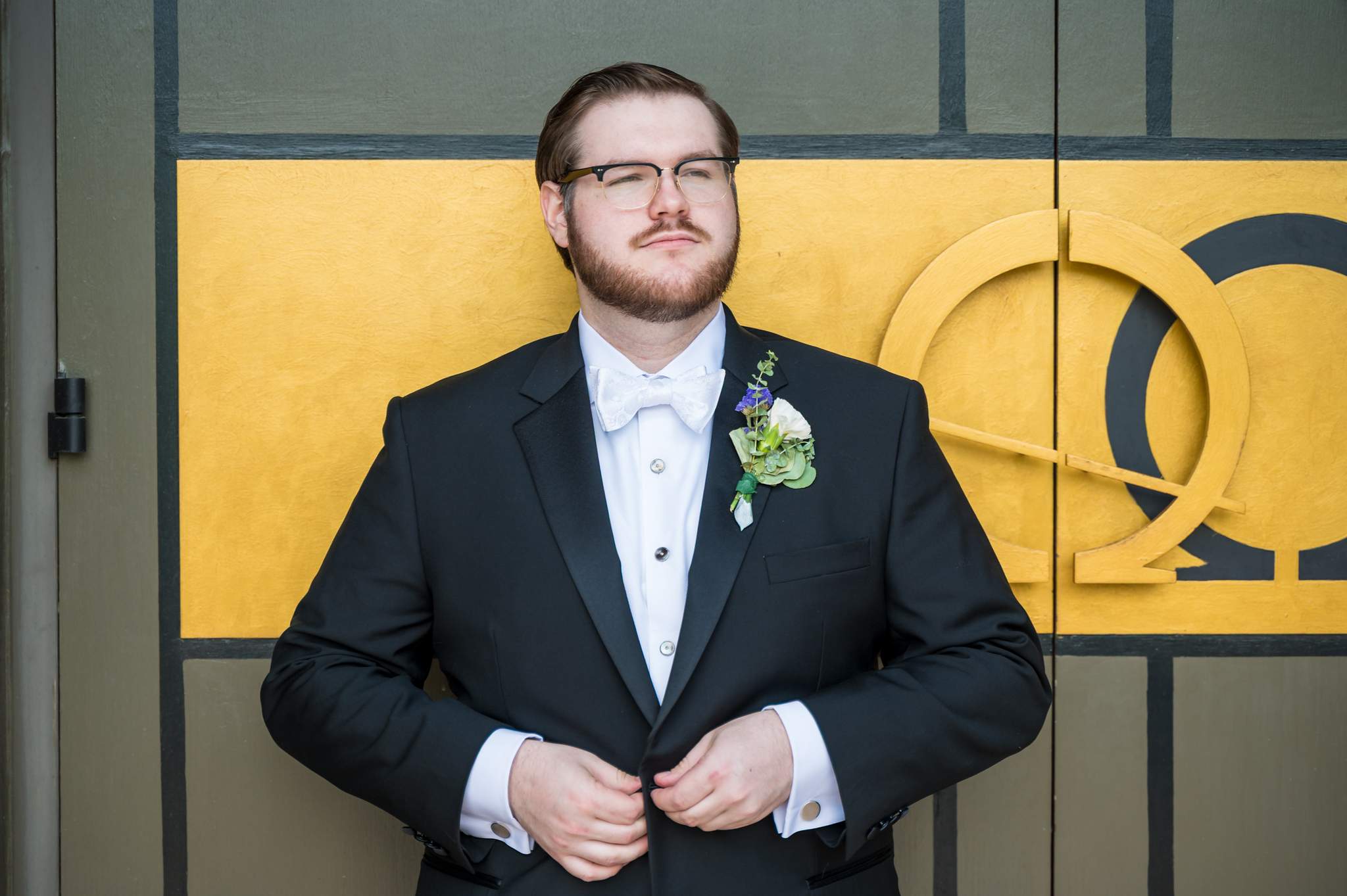 Groom buttoning his jacket in front of the gold church doors at Immaculate Heart of Mary