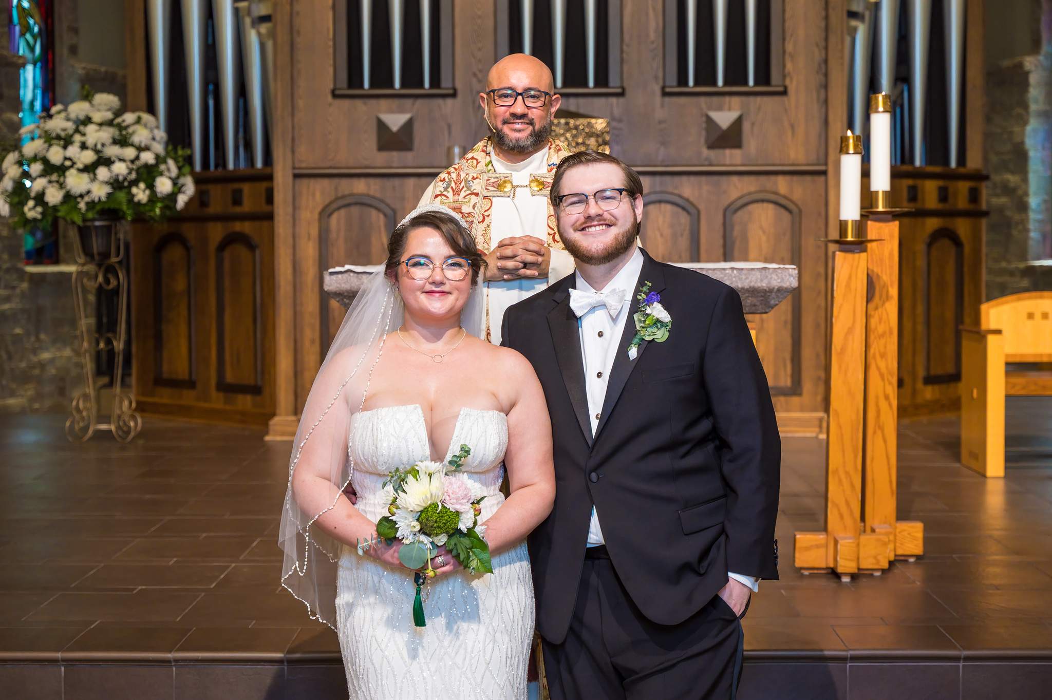 Couple with the priest at the altar after their ceremony at Immaculate Heart of Mary