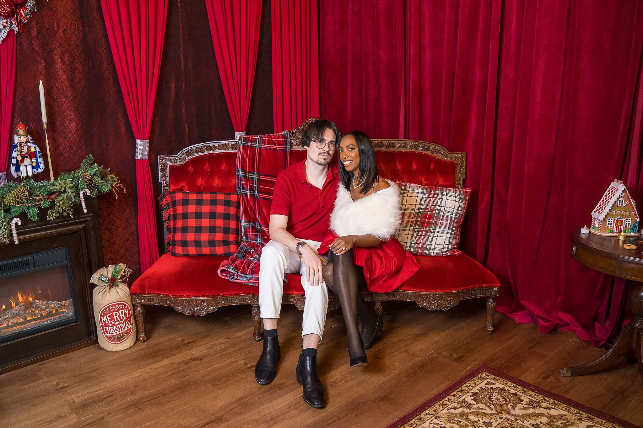 Couple seated on a red velvet sofa on a Christmas set at Luxe Galore Studios Atlanta