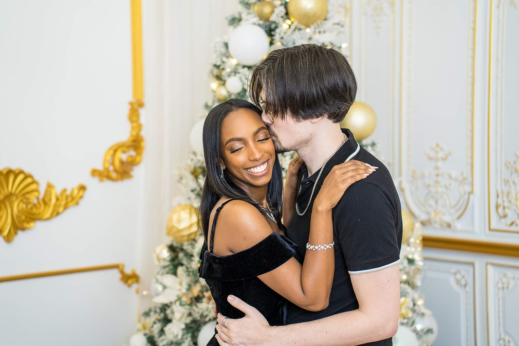 Newly engaged couple embracing beside a gold and white Christmas tree at Luxe Galore Studios Atlanta