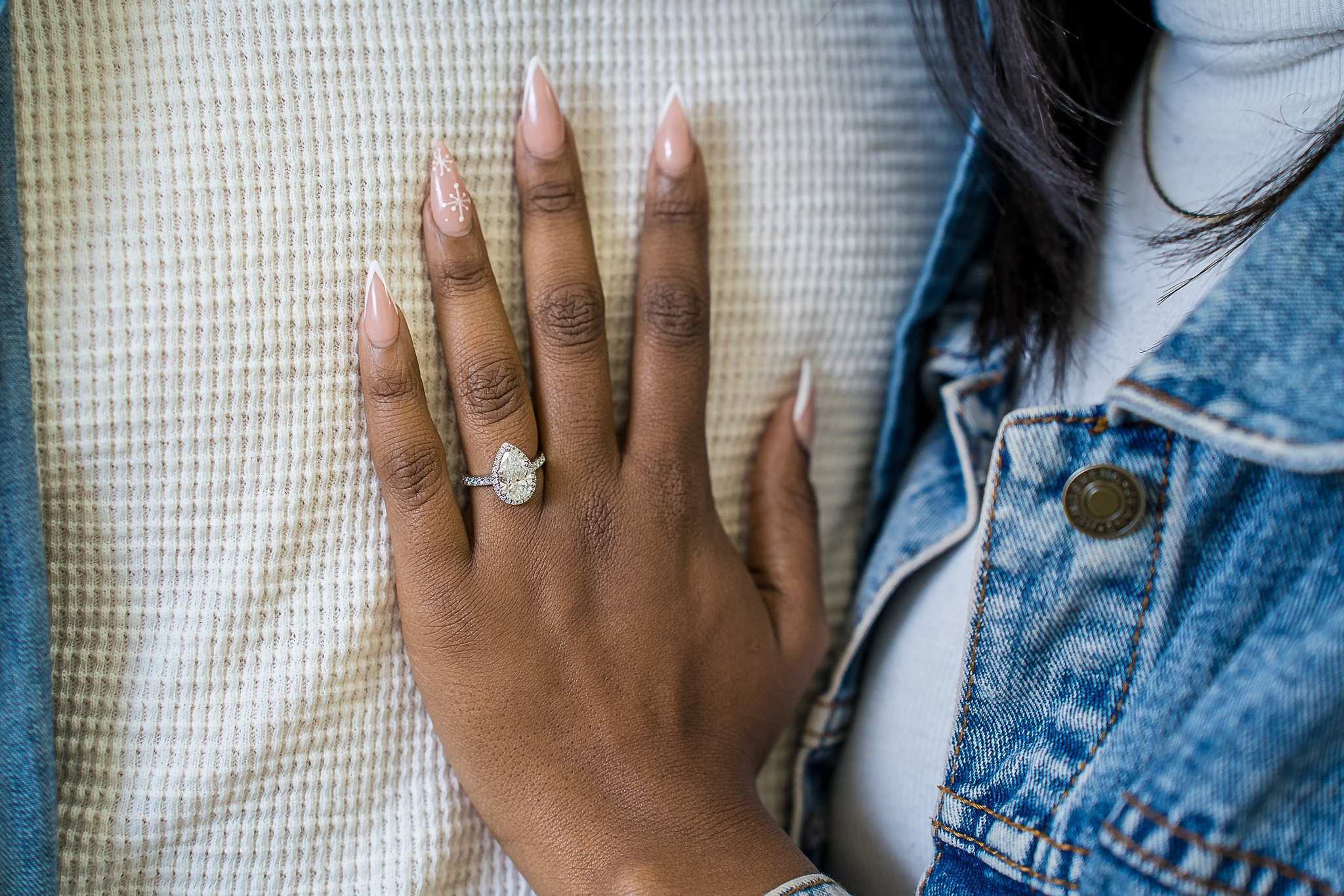 Close-up of an engagement ring on a hand resting on a denim jacket