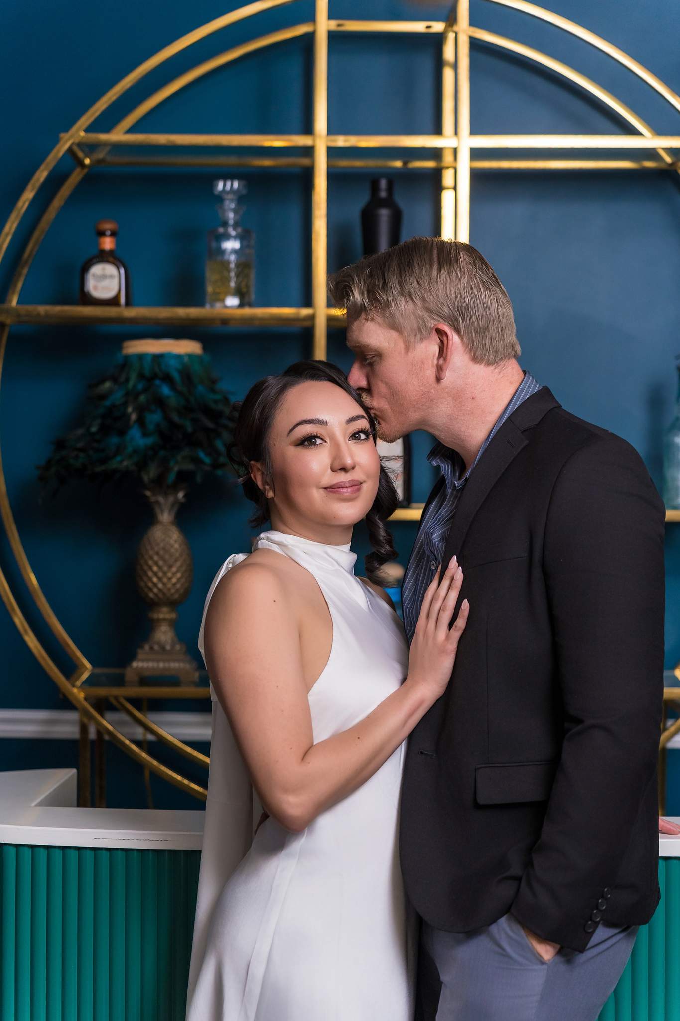 Man kissing his partner's temple in front of gold shelving at Luxe Galore