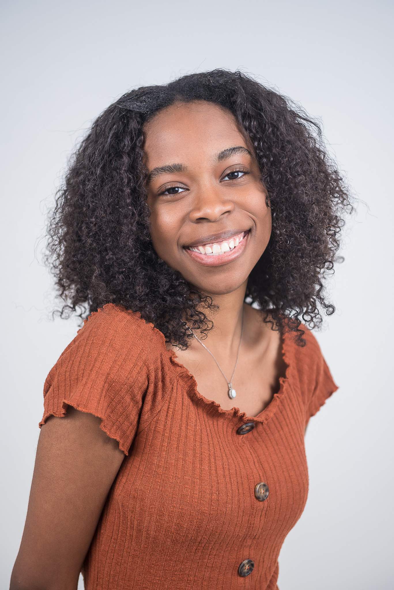 Smiling woman in a rust top in front of a white wall at White Wall Studio Woodstock